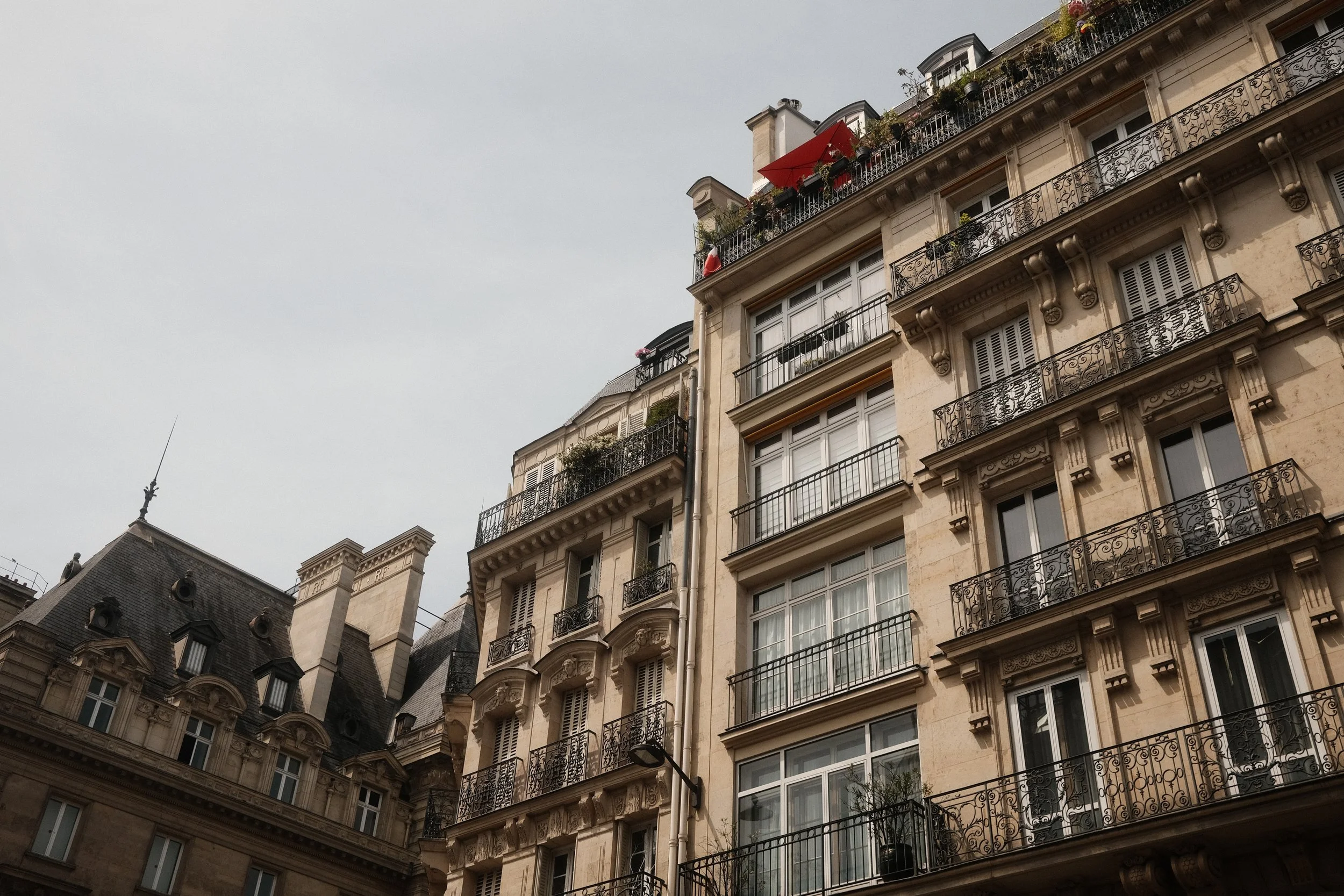 Image of classic European-style residential buildings with ornate balconies and a rooftop terrace, under cloudy sky.