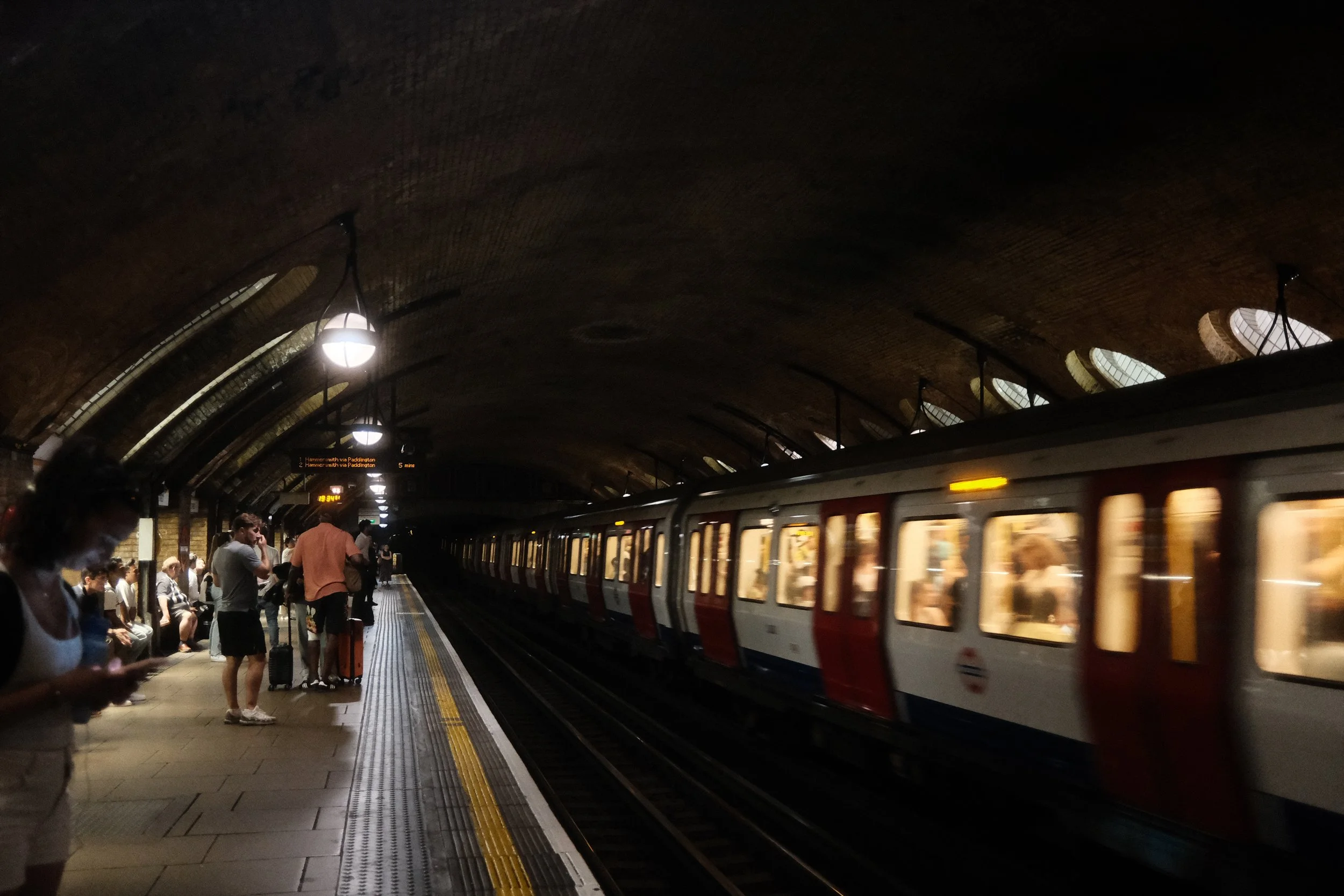 Underground train arriving at a subway station with passengers waiting on the platform and some people using their mobile phones.