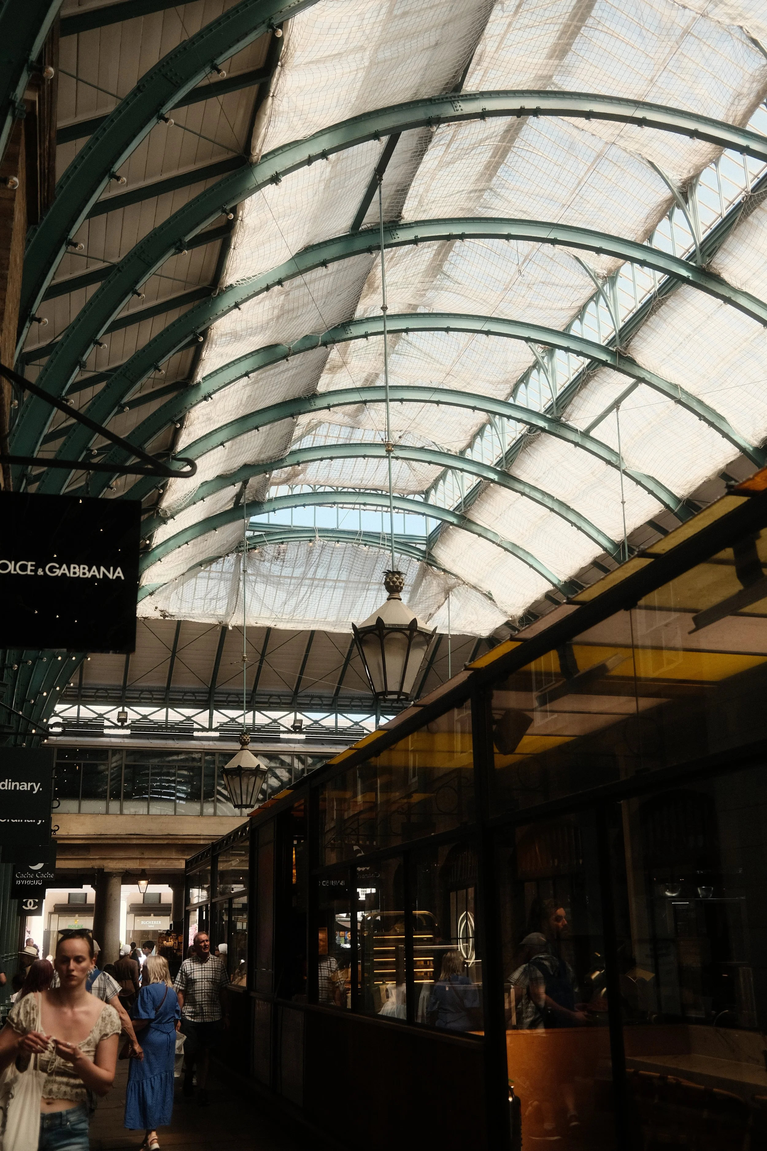 Crowd of people walking inside a shopping mall with a glass and metal arched ceiling, and storefronts, including a Dolce & Gabbana store.