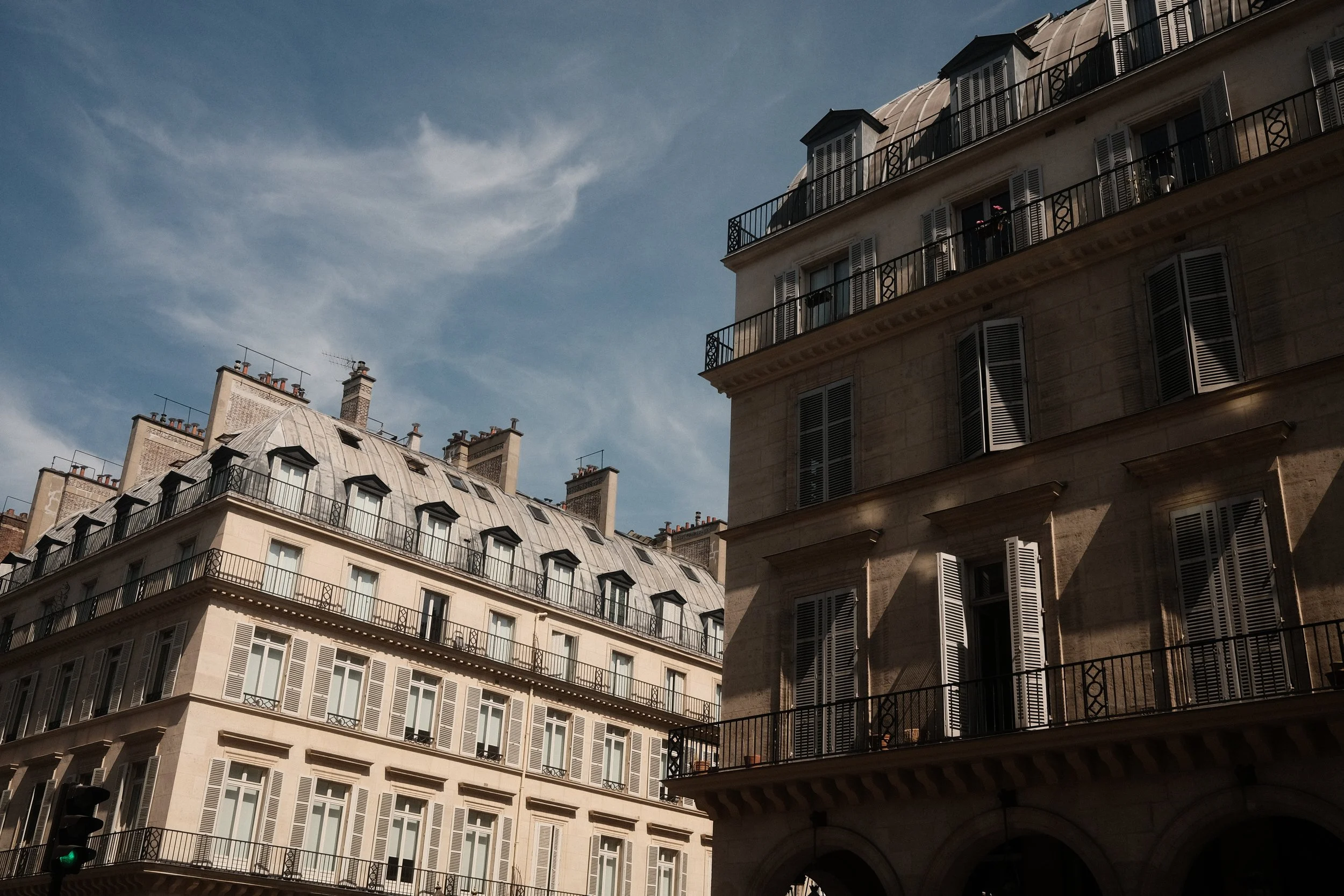 Parisian apartment buildings with gray roofs, ornate balconies, and tall windows, against a blue sky with wispy clouds.