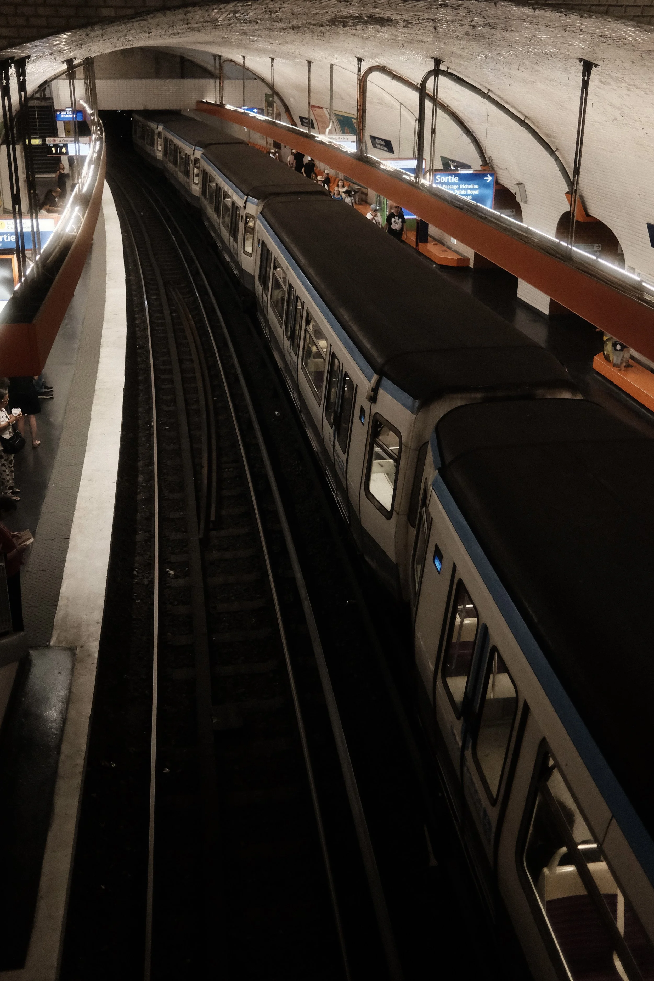Underground subway station with a train stopped on the platform and passengers waiting to board.