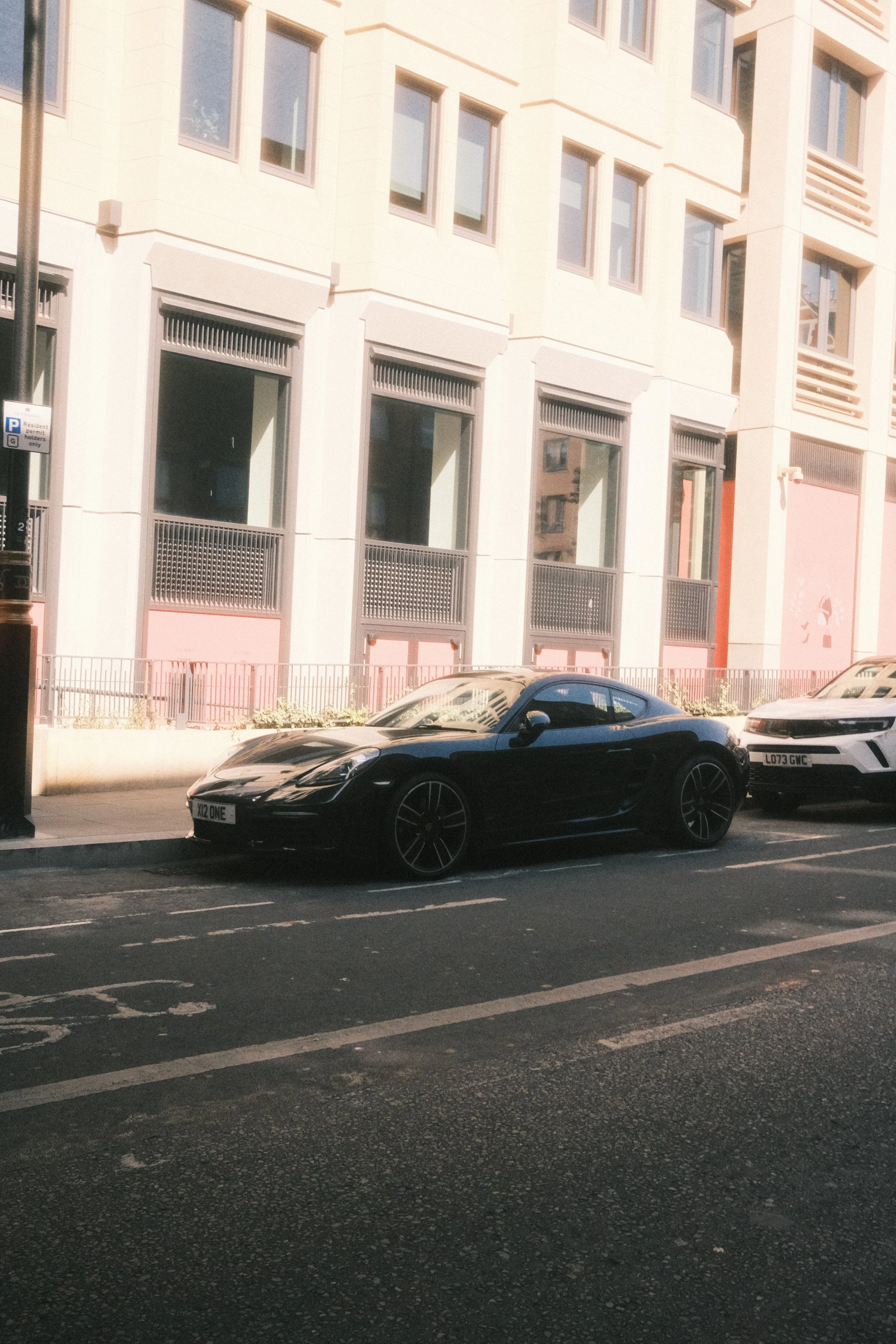 A black sports car parked on the street in front of a modern beige building with multiple windows and balconies.
