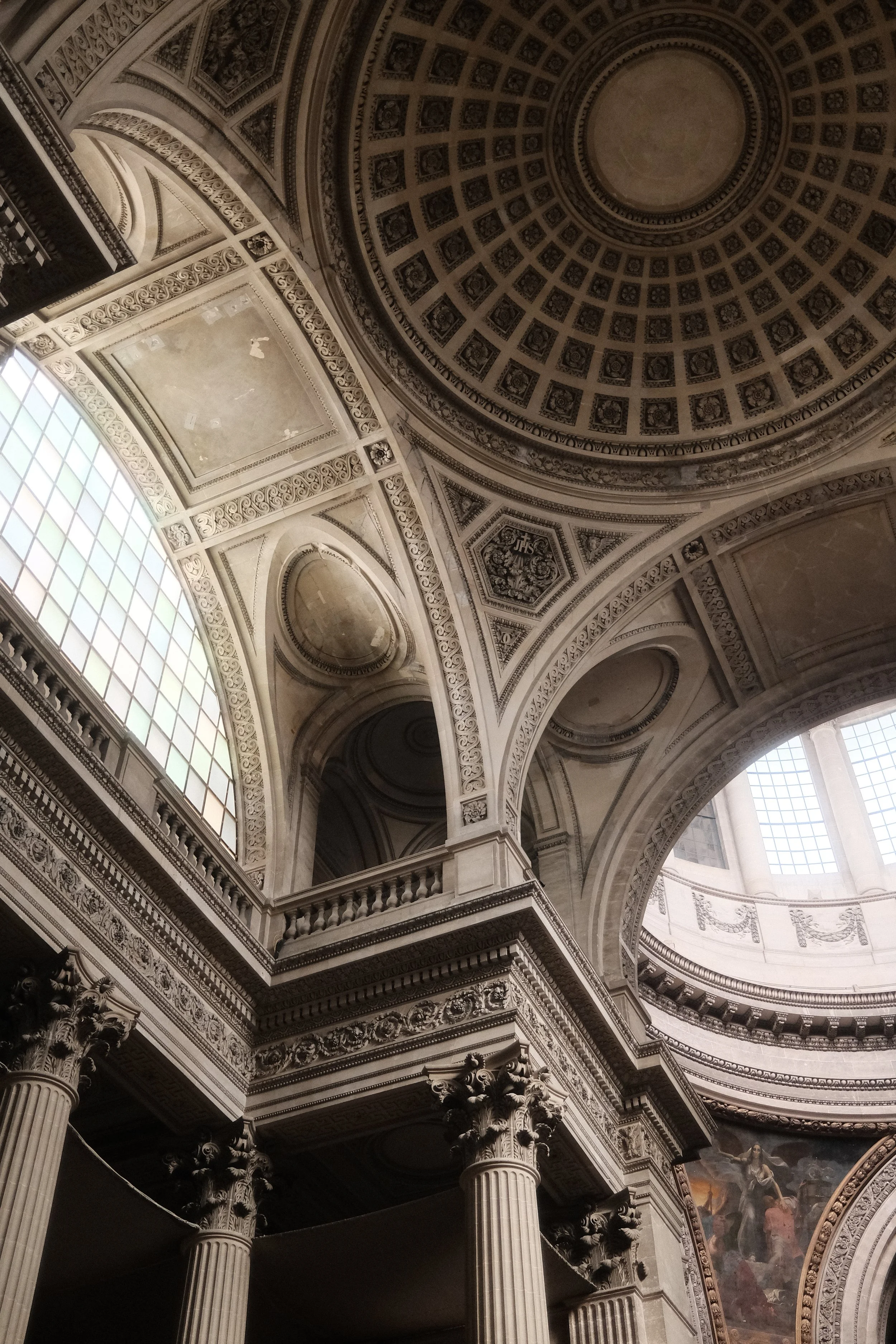 Interior of a historic church or cathedral with ornate architectural details, including large columns, decorative arches, intricate cornices, and a domed ceiling with patterned squares and a central fresco. Natural light enters through large windows.