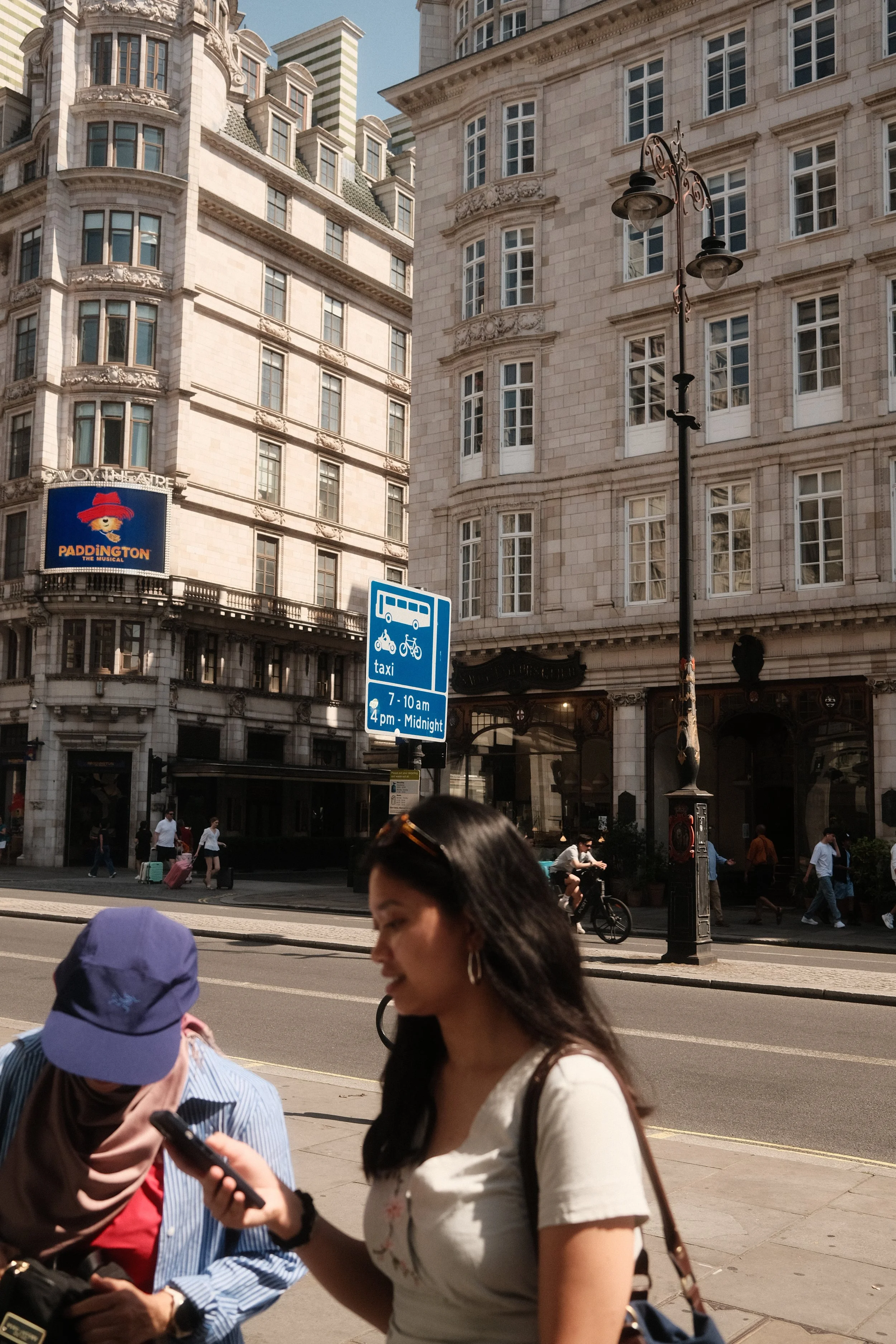 Street scene in a city with historic buildings, pedestrians, cyclists, and street signs indicating bus and taxi zones.