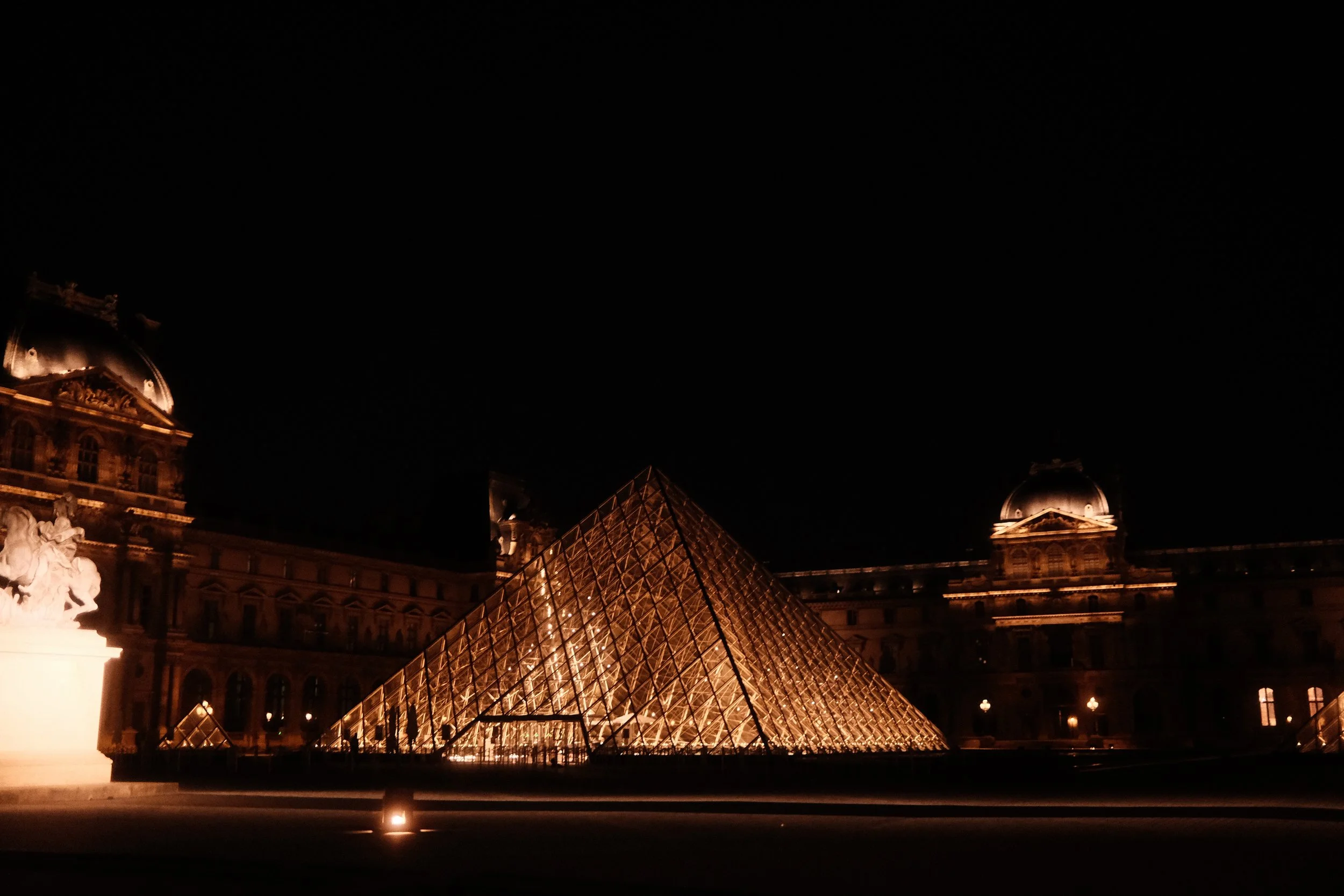 Night view of the illuminated Louvre Museum in Paris, France, with its glass pyramid in the foreground and historic buildings in the background.