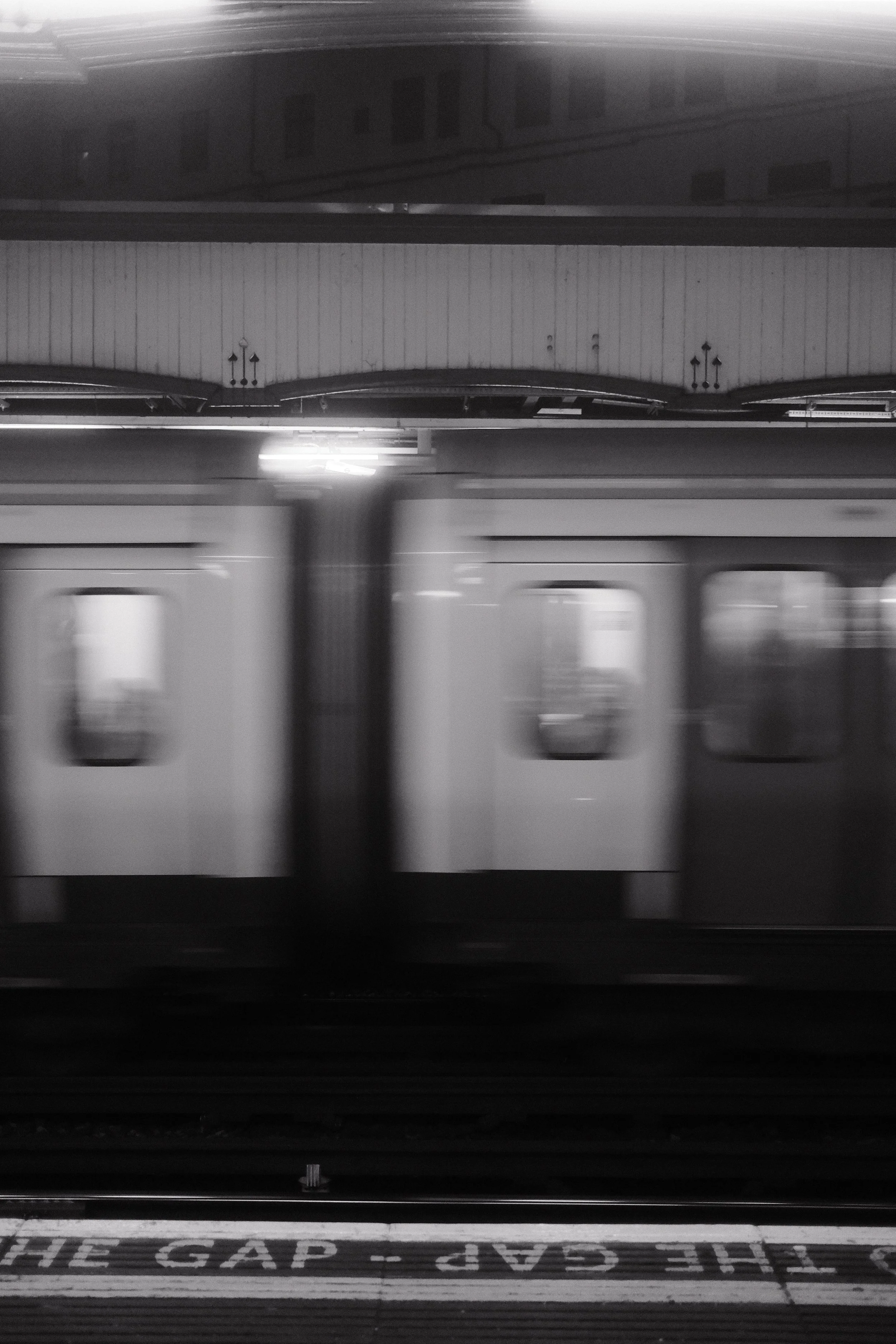 A black and white photo of a train at a station with the words "STOP THE GAP - PLEASE" on the platform