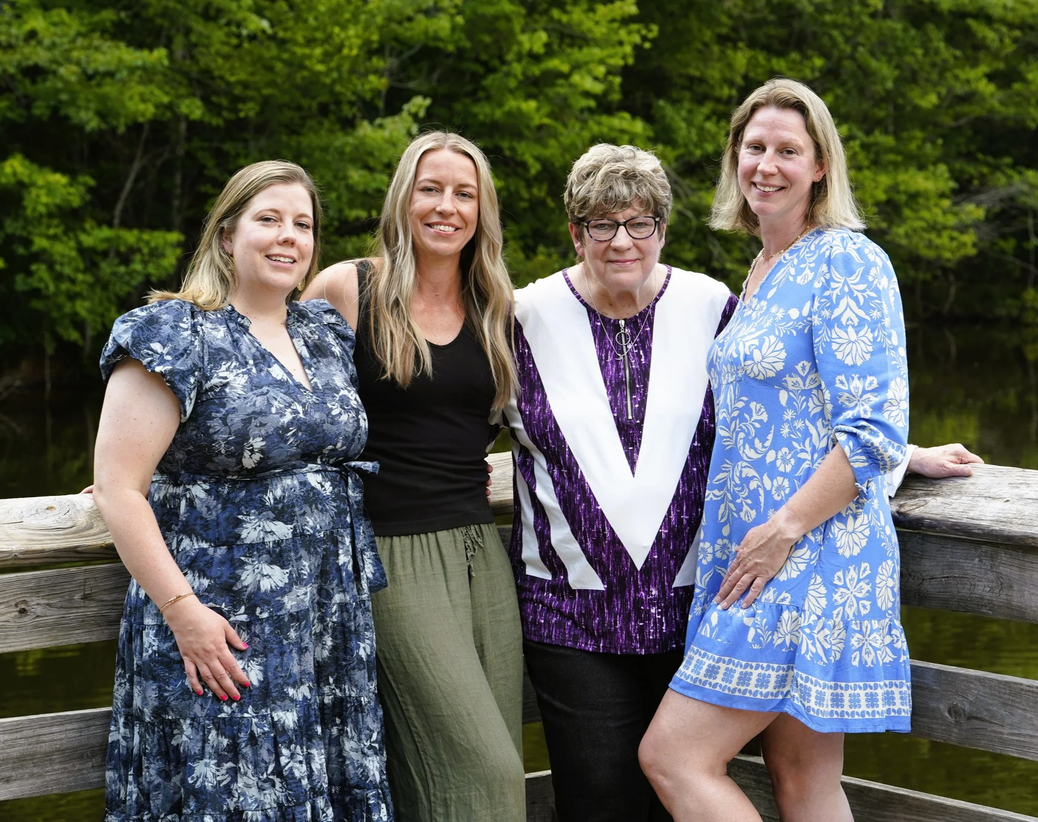 A Raleigh photographer's photo for a mother's day shoot of mom and daughters for a family photos against a background of trees on a wooden dock of a pond at Seagroves Park, Apex, North Carolina