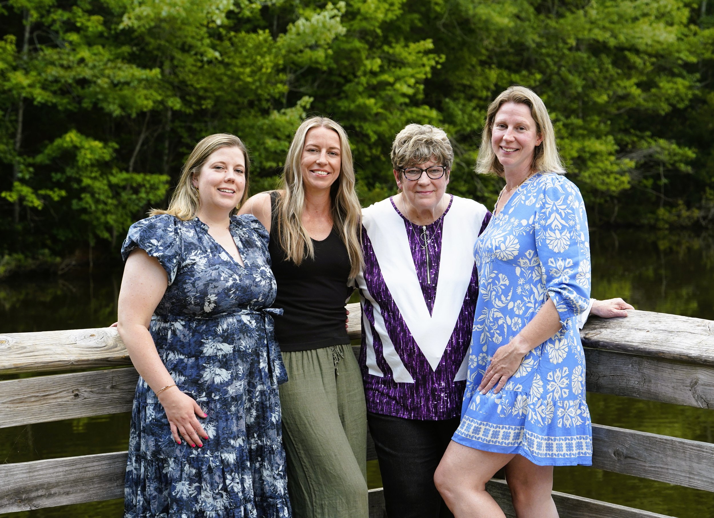 A Raleigh photographer's photo for a mother's day shoot of mom and daughters for a family photos against a background of trees on a wooden dock of a pond at Seagroves Park, Apex, North Carolina