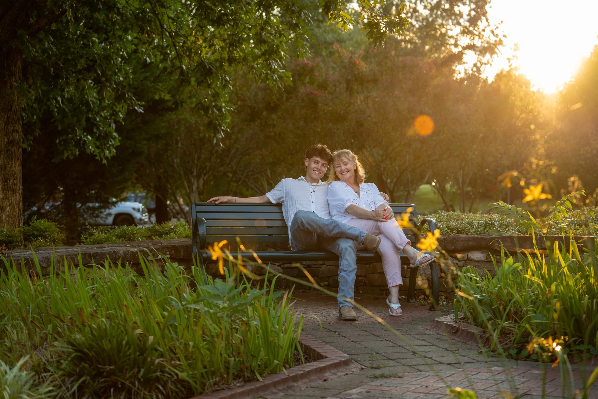 A mother and son sit together at sunset with foliage and blooming flowers highlighting the photos for outdoor senior and family photos in Raleigh, North Carolina