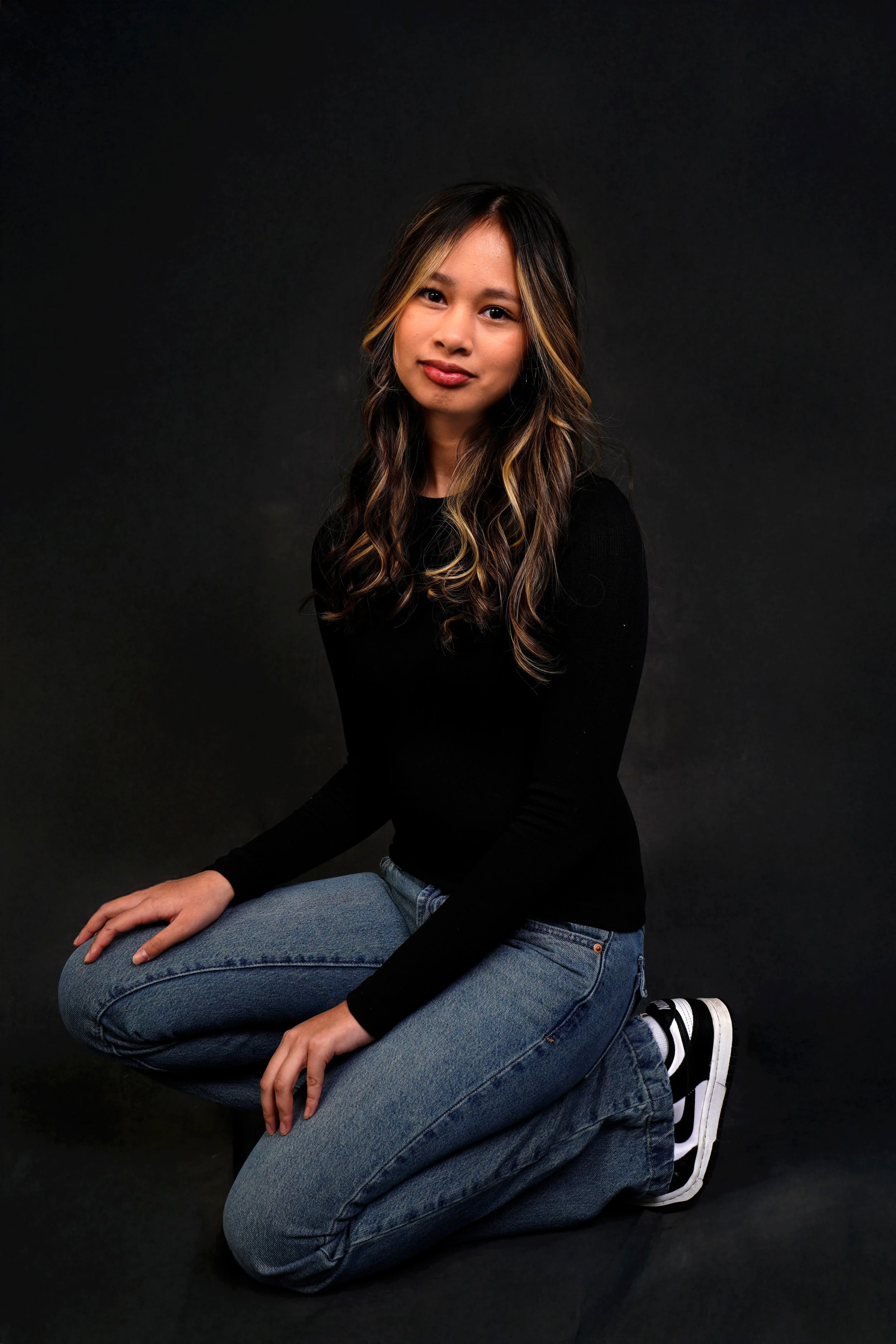 A woman's kids casting photo taken in a Raleigh photography studio for modeling and acting portfolios with her kneeling in jeans and a black shirt against a black background