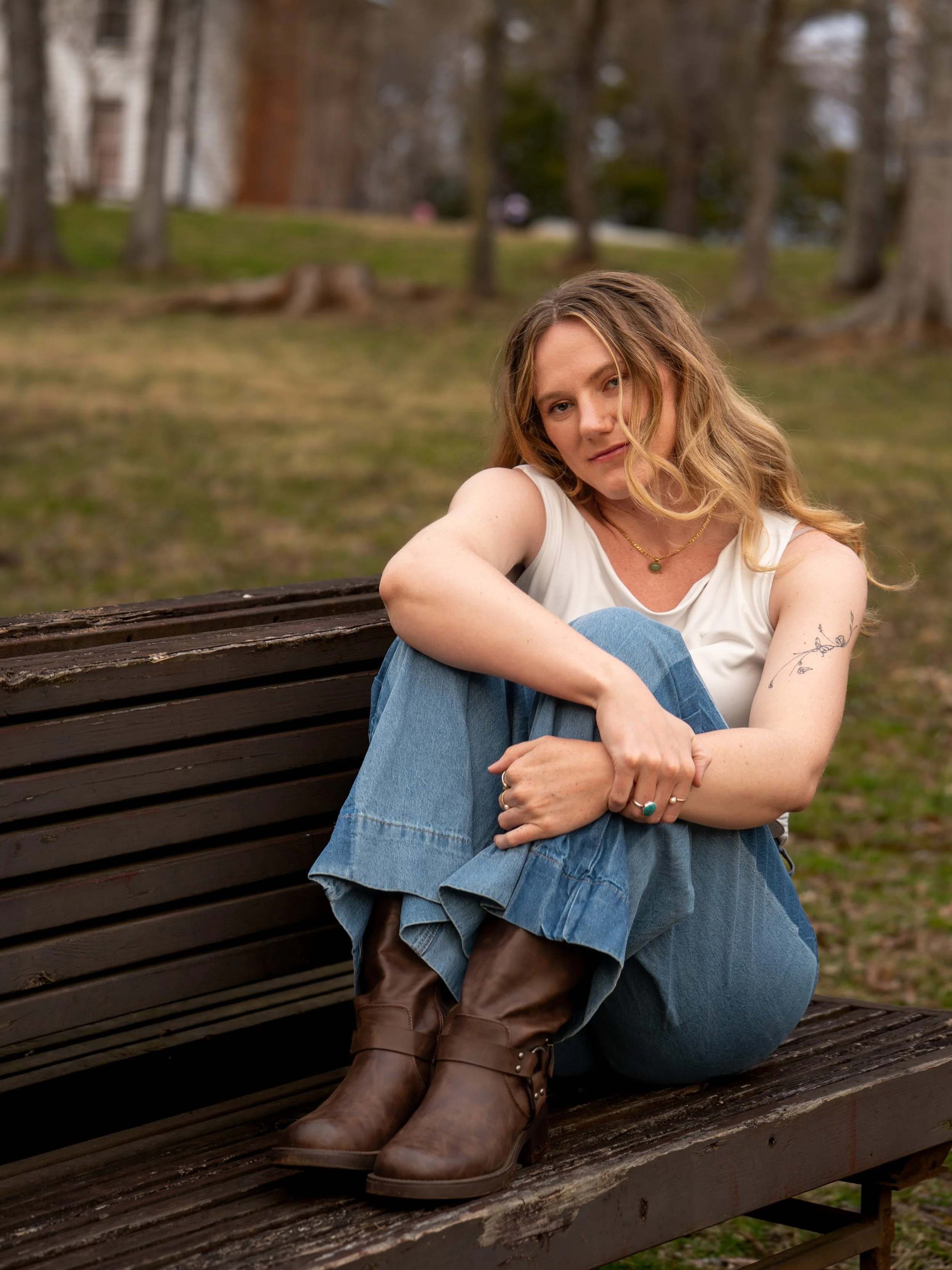 A young woman in a white top and blue jeans poses on a wooden pinch with her hair flowing beside her face at West Point on the Eno Park, Durham North Carolina for High School Senior Photos