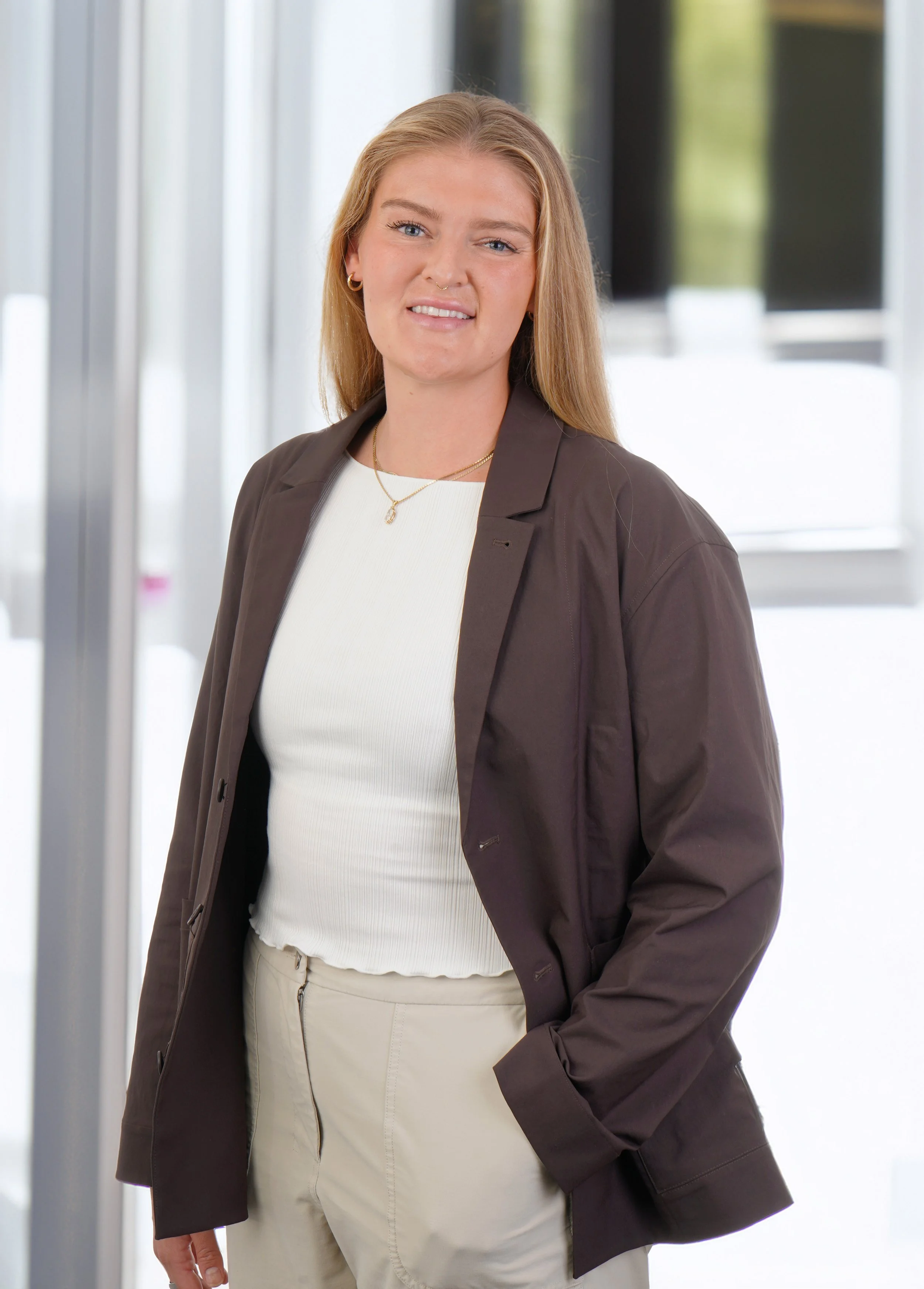 A young woman poses in a confident posture, hands in pockets with an office background that gives it a young look in Cutting Edge Raleigh Photography Studio