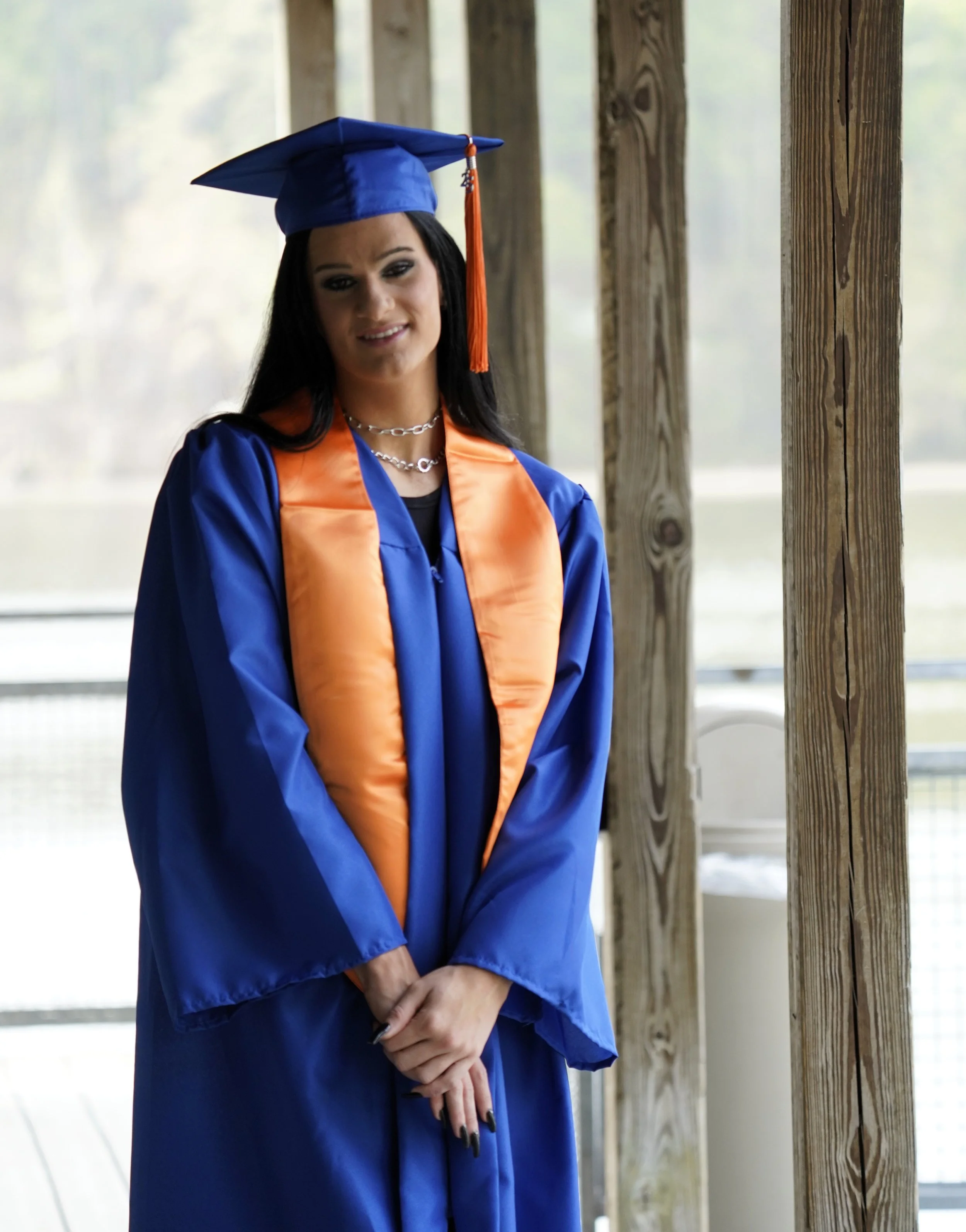 A woman stands in her graduation regalia at Lake Crabtree for her senior photos, Raleigh, North Carolina. High School Senior Photography.