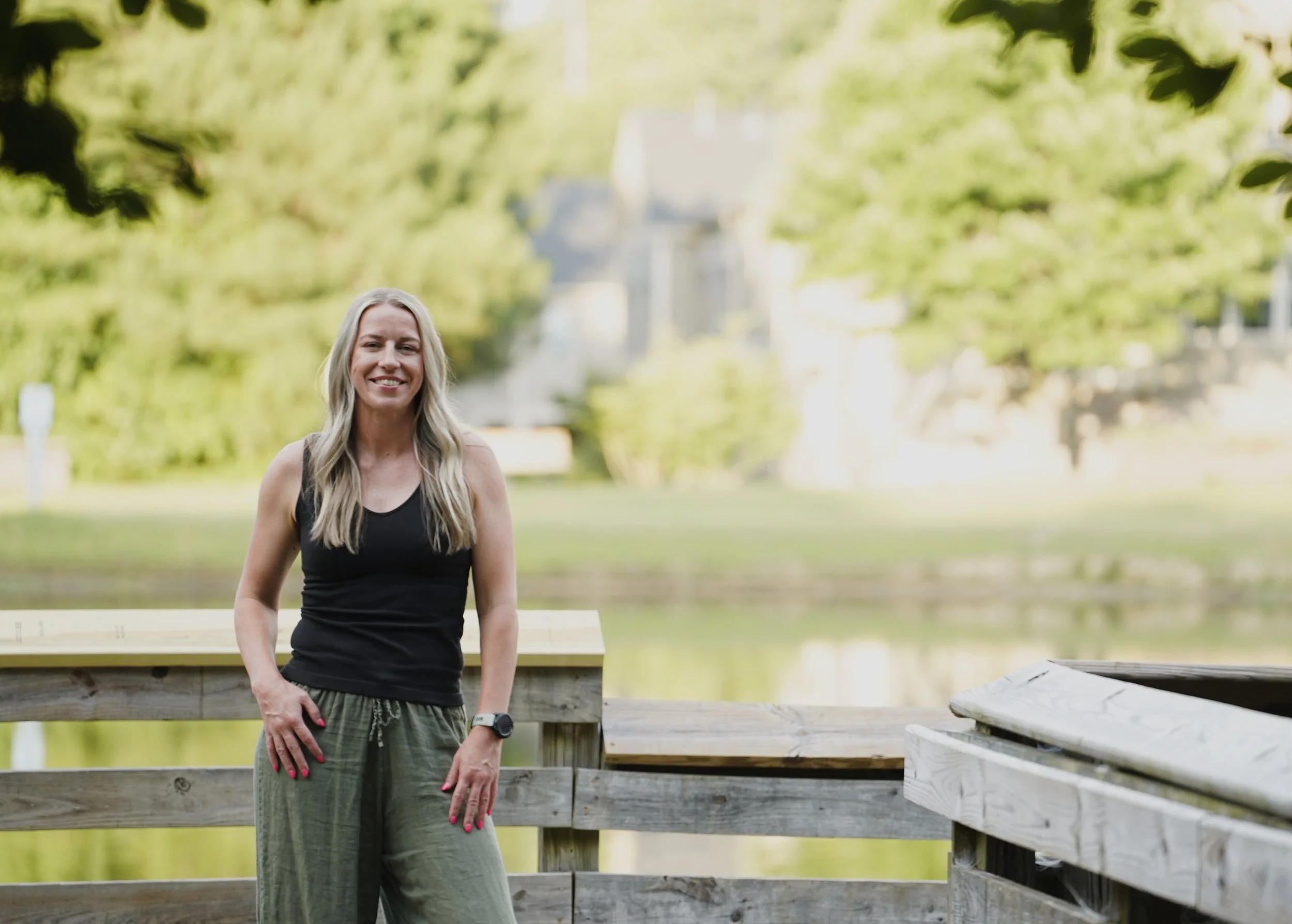 A young woman poses for a creative outdoor portrait against a bright backdrop of trees and water at Seagroves Park, Apex, North Carolina