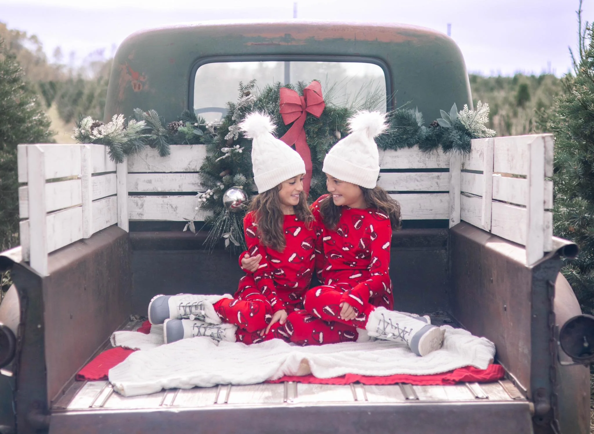 Outdoor Christmas mini session at a tree farm near Omaha—two children in matching red pajamas with evergreens behind them