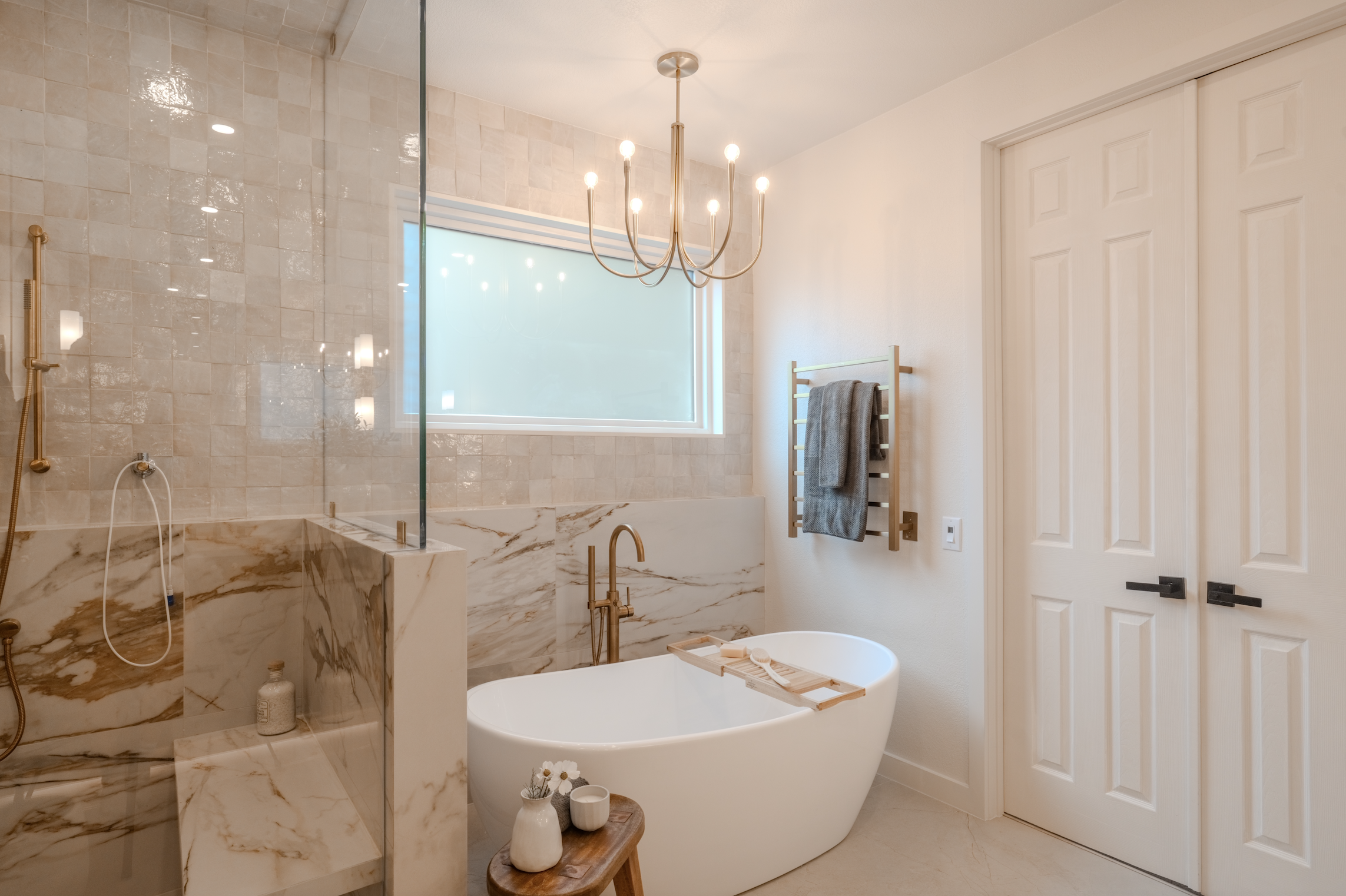 Modern bathroom with a freestanding bathtub, marble accents, glass-enclosed shower, large window, and minimalist decor.