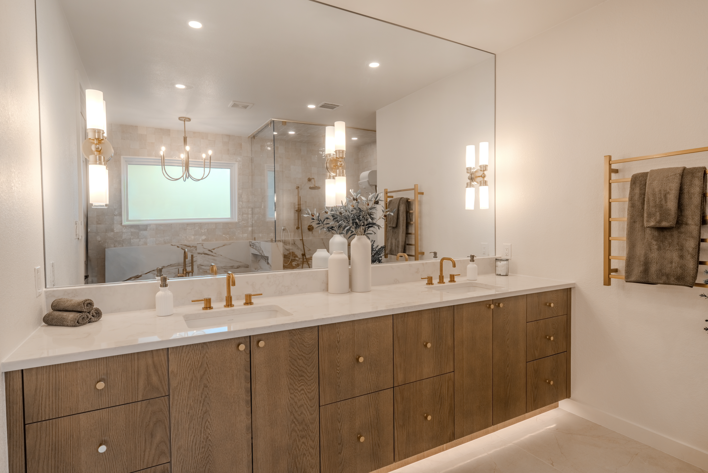 Modern bathroom with double vanity, gold fixtures, large mirror, and a walk-in shower with glass enclosure.