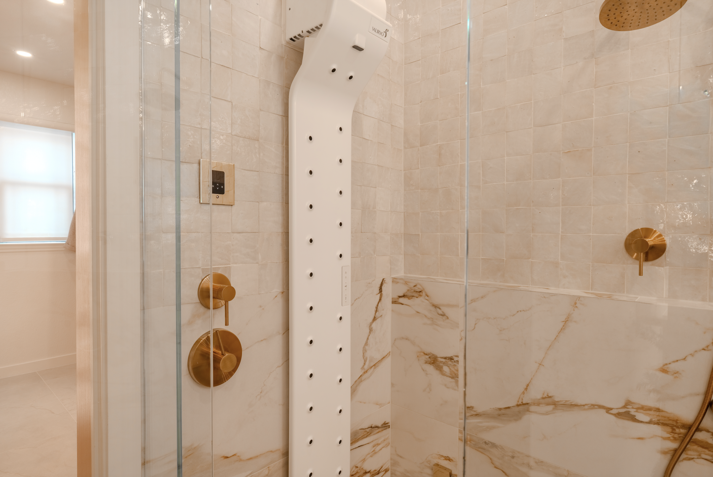 Shower with marble tiles, gold fixtures, glass doors, and a white steam generator panel.