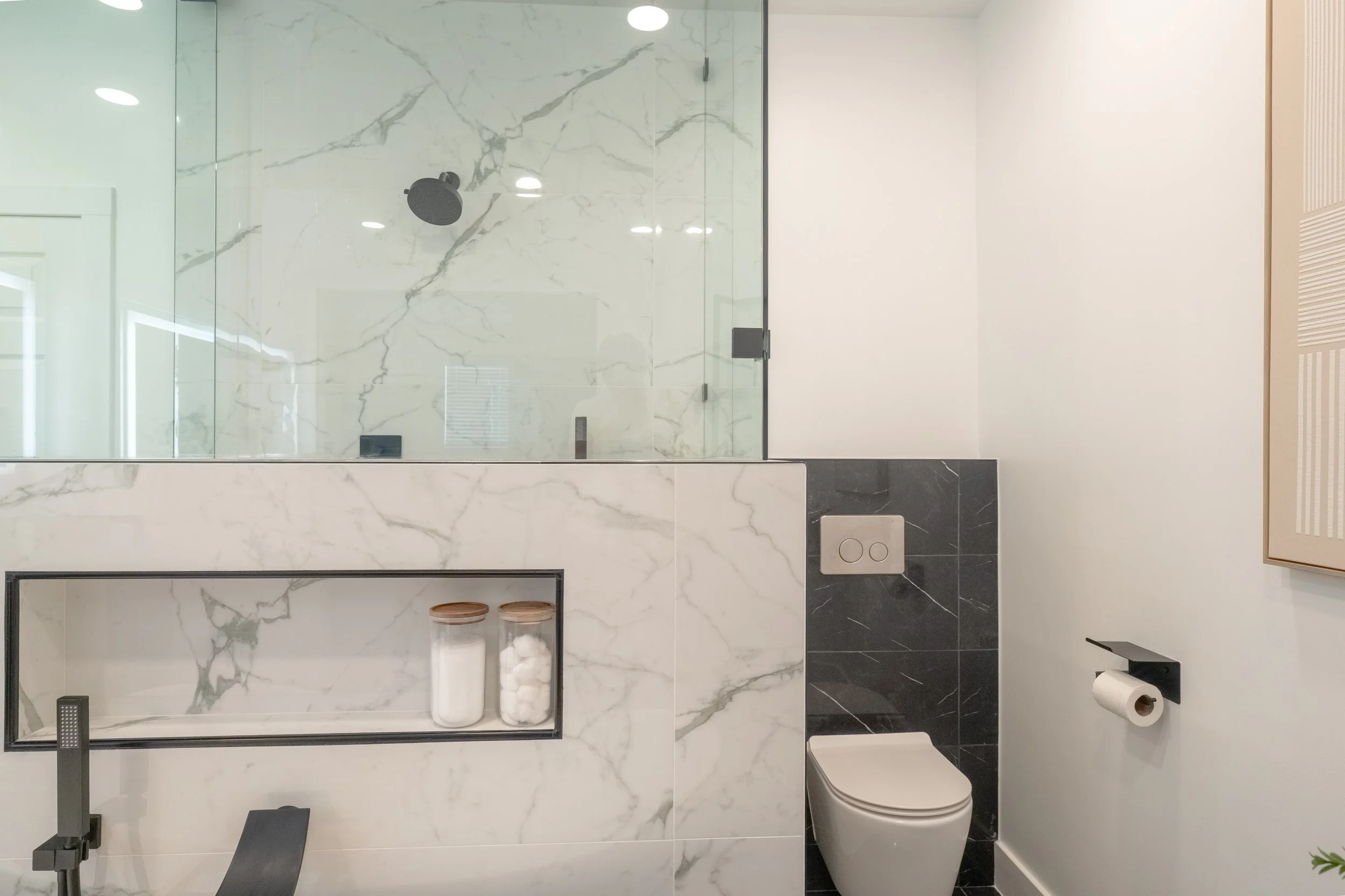 Modern bathroom with a shower area enclosed by glass, marble tiles, a wall-mounted toilet, and a tissue holder.