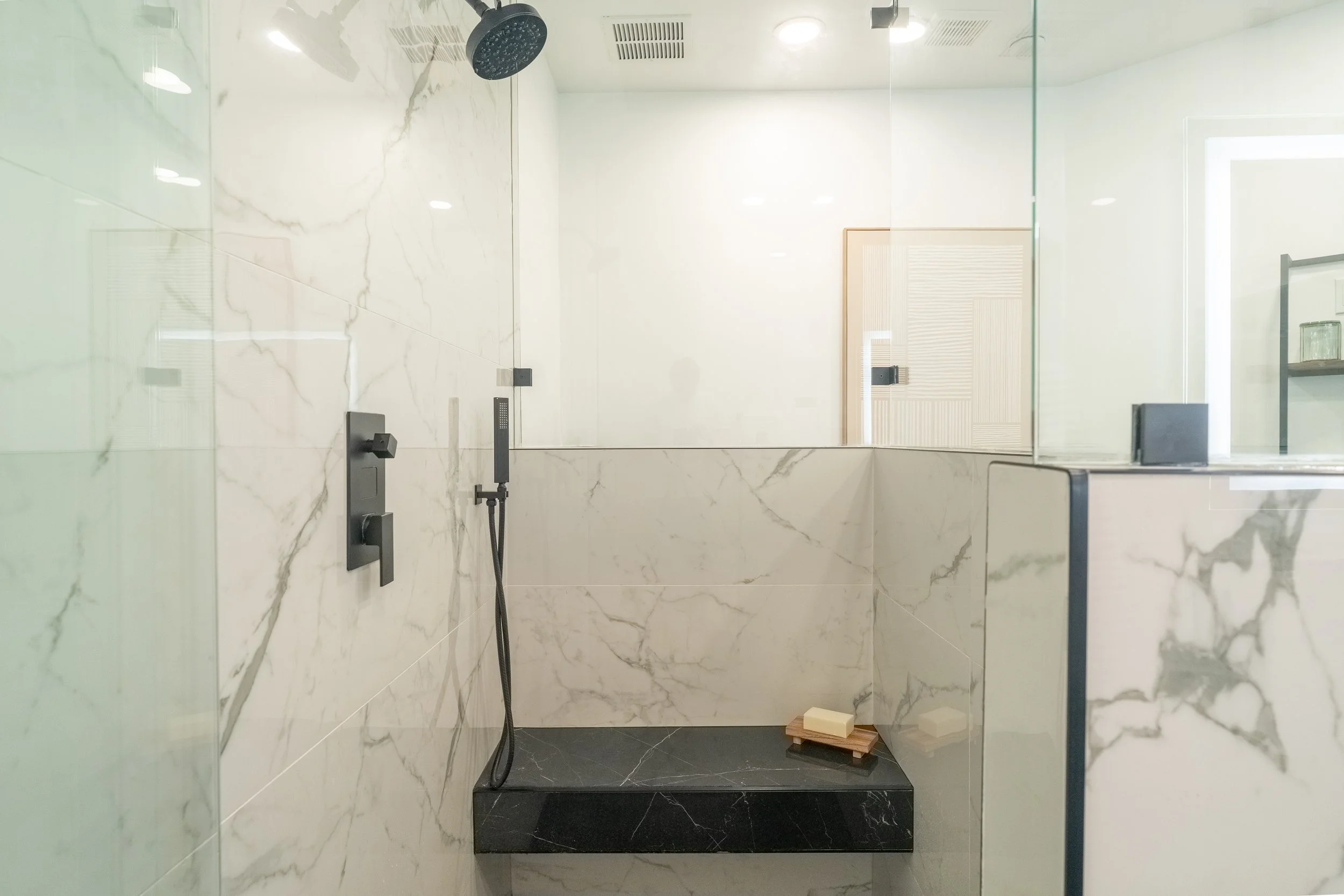Modern shower area with marble walls, black fixtures, and a glass partition.