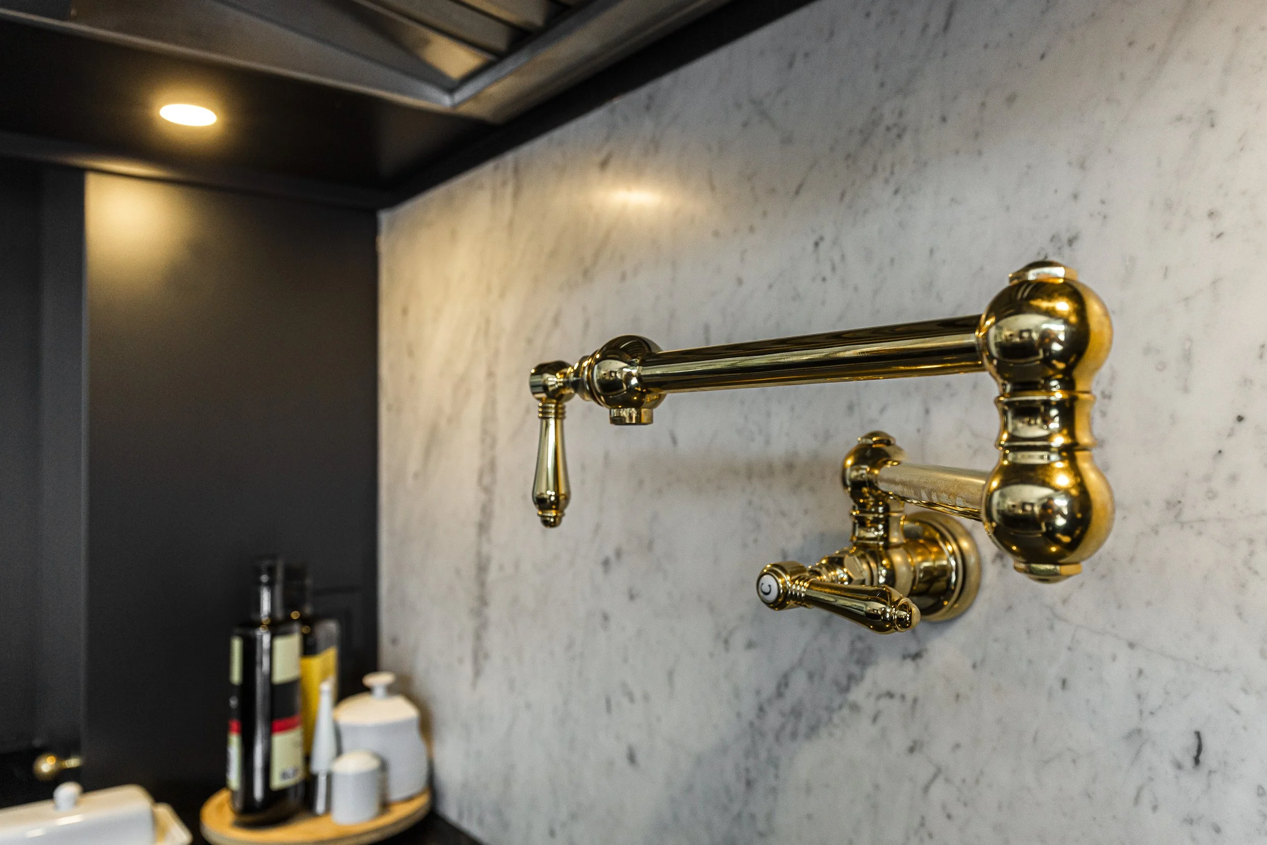 Close-up of a gold-colored wall-mounted faucet with a showerhead attachment, set against a marble wall in a modern bathroom.