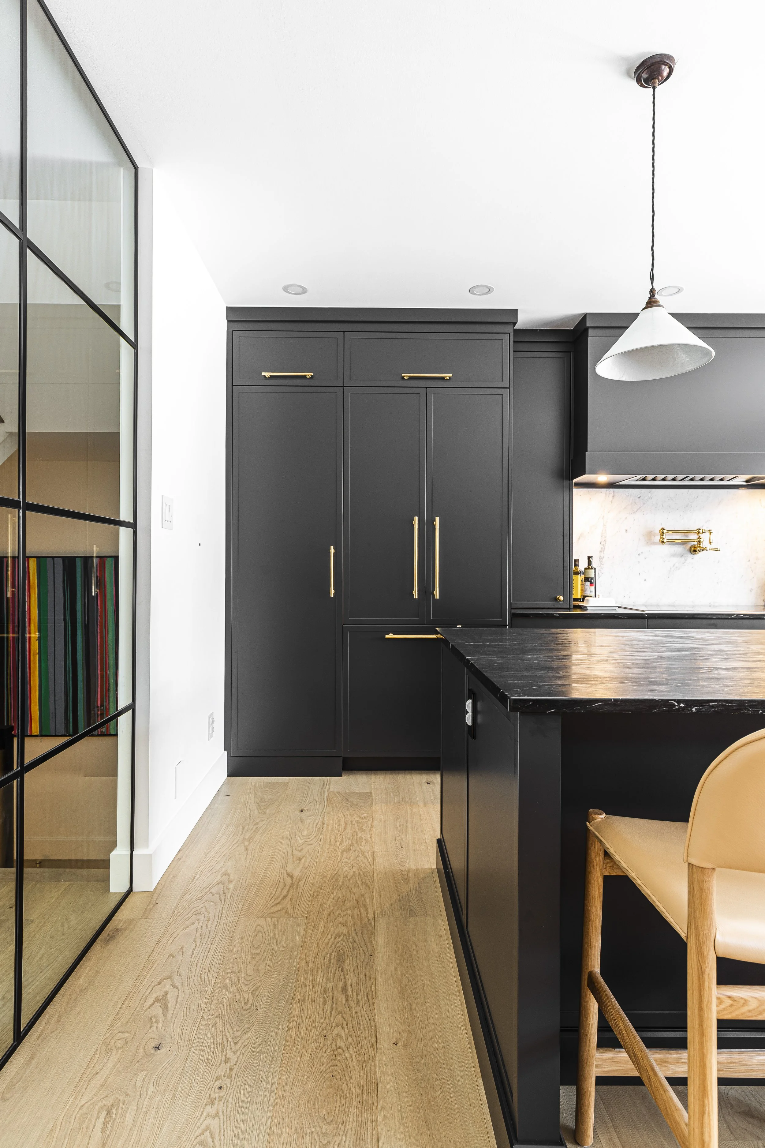 Modern kitchen with dark gray cabinets, black marble countertop island, wooden flooring, and a white pendant light.