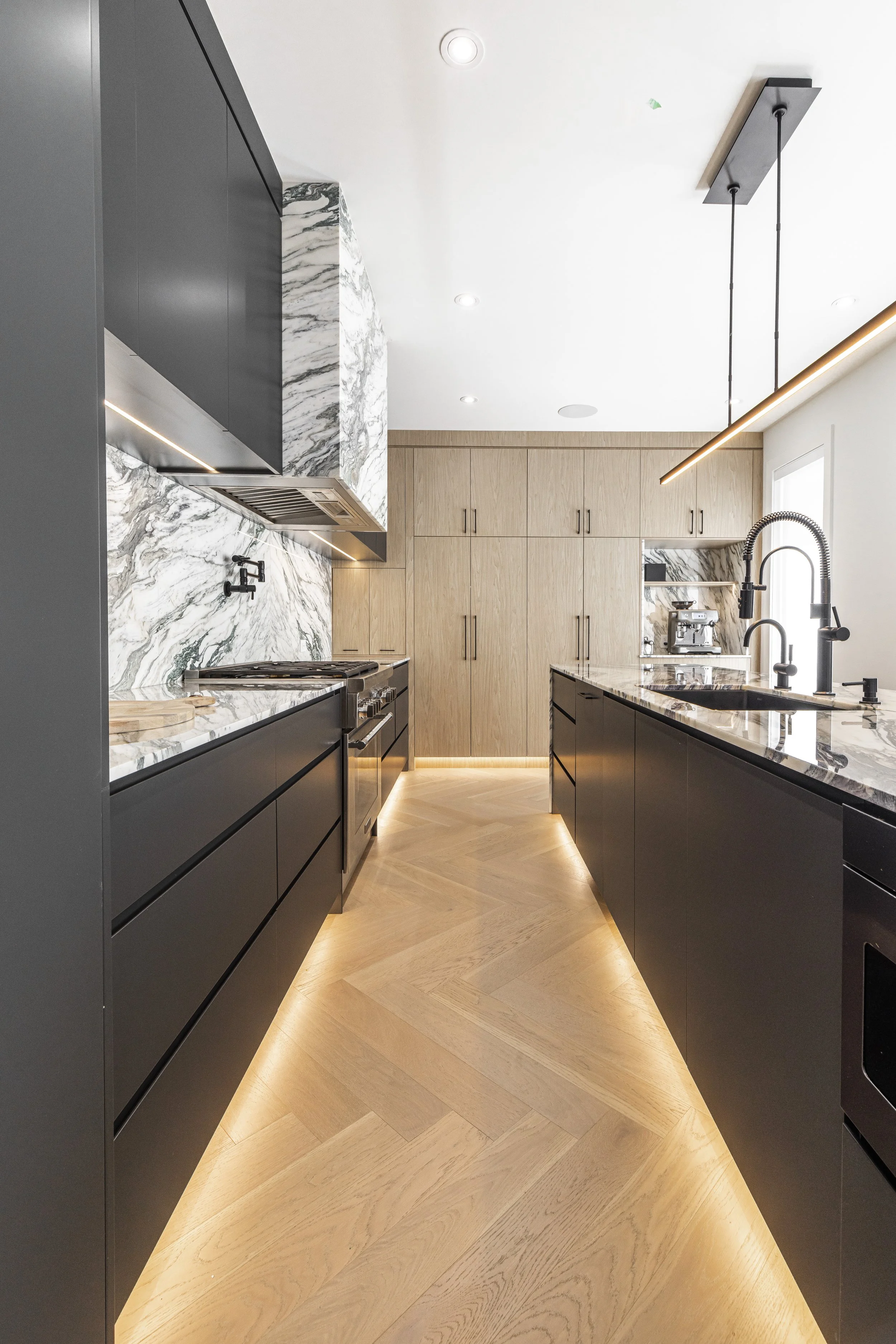 Modern kitchen with black and wood cabinetry, marble countertops, and under-cabinet lighting.
