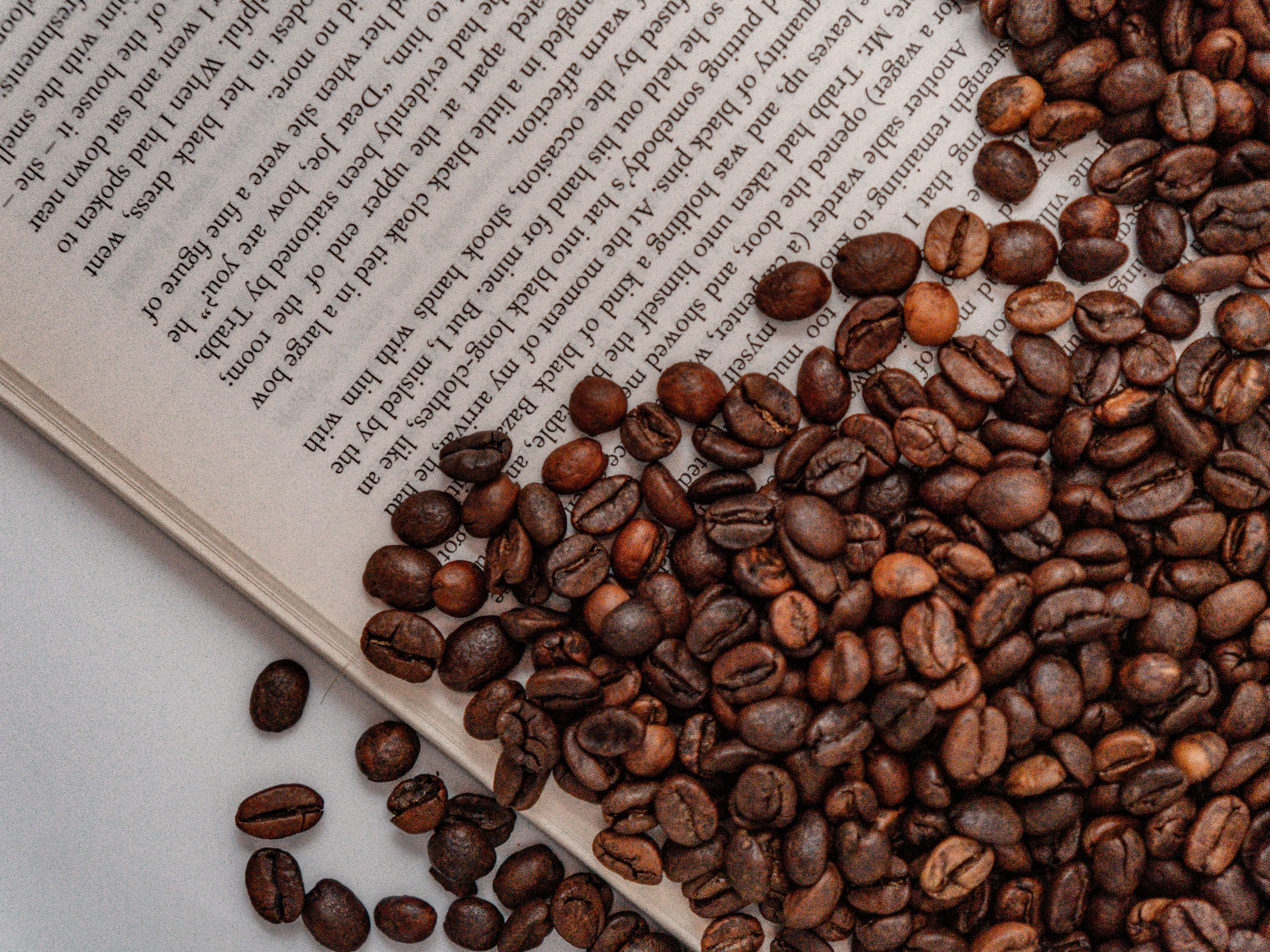 Coffee beans scattered over an open book with visible text.