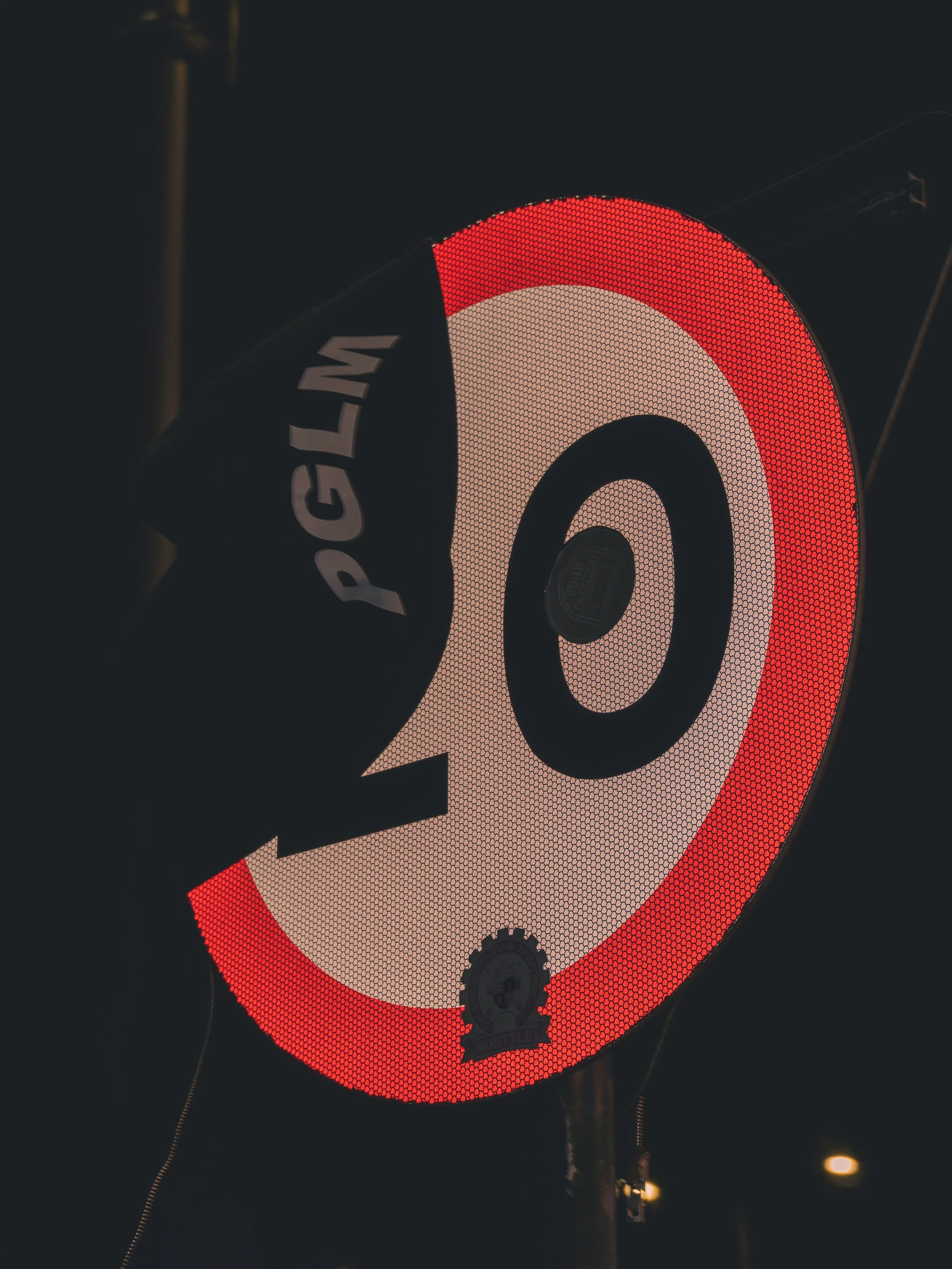 Illuminated circular speed limit traffic sign displaying a limit of 20 miles per hour, with a reflective surface and a black and red border, at night.