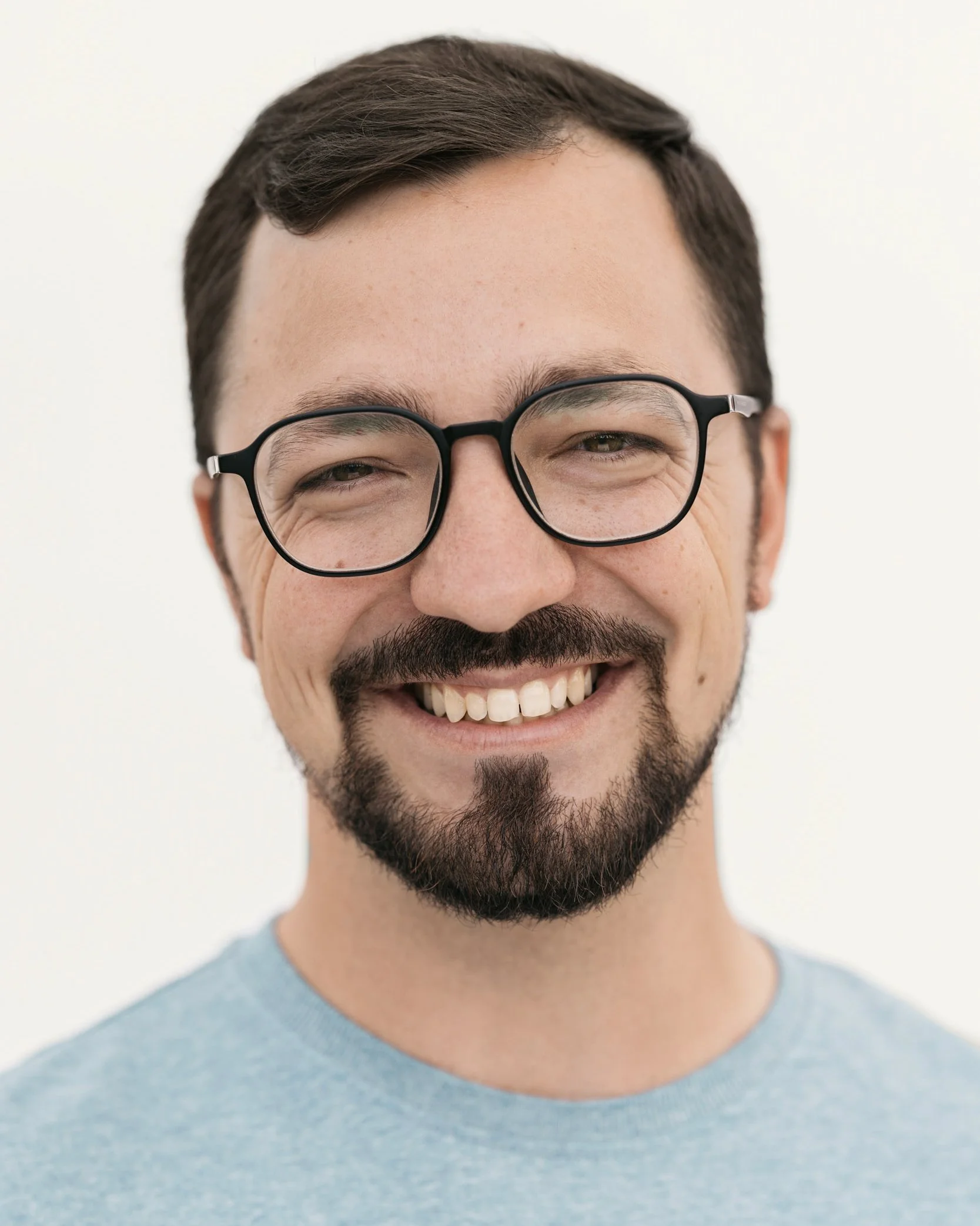 Smiling bearded man wearing black eyeglasses and a light blue shirt