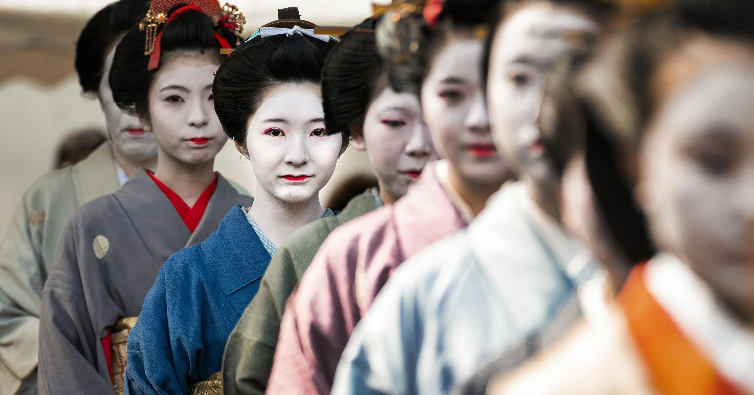 Geisha women in traditional Japanese kimono and elaborate hairstyles standing in a line