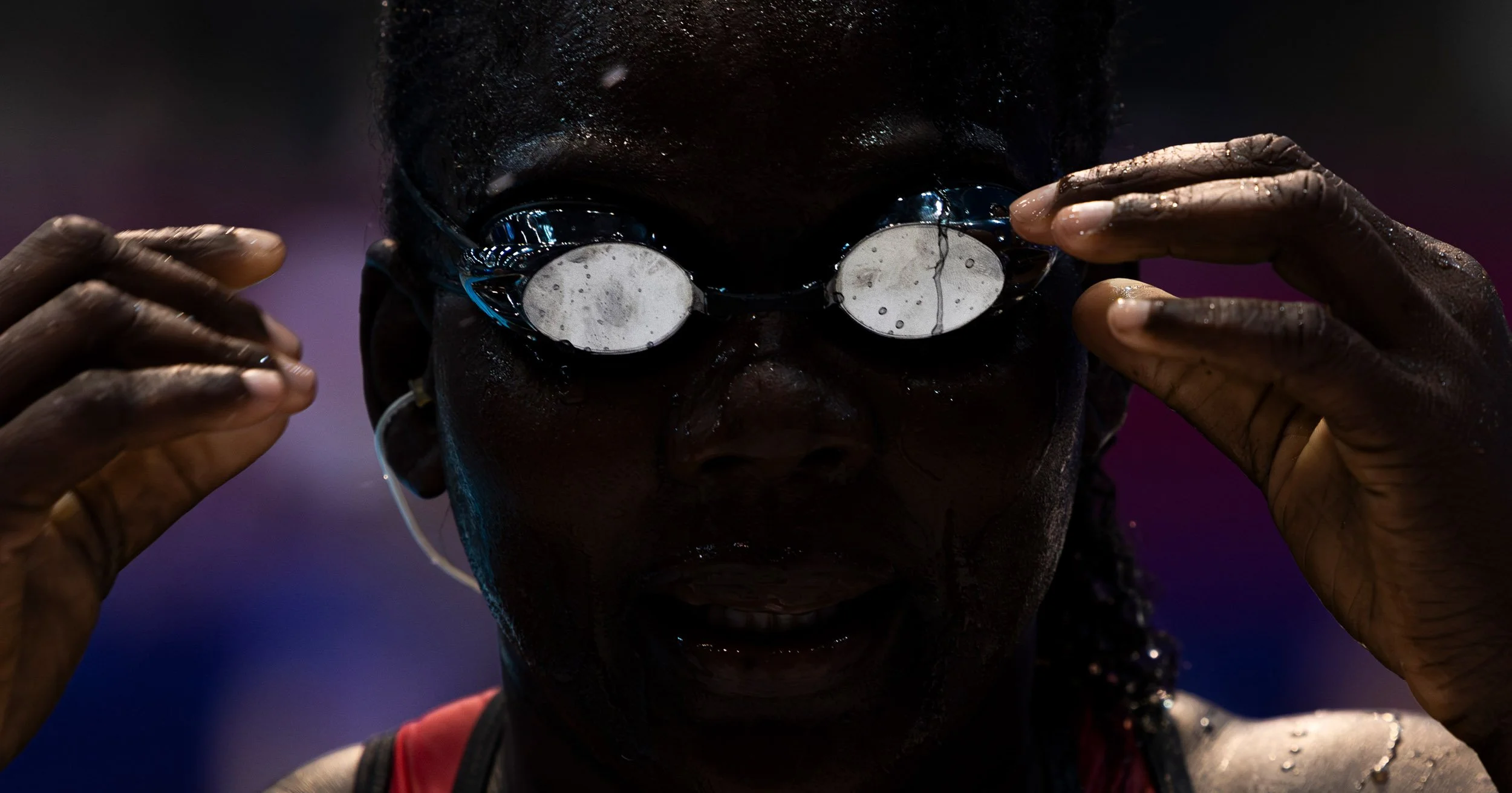 Close-up of a man adjusting reflective sunglasses under purple and blue lighting