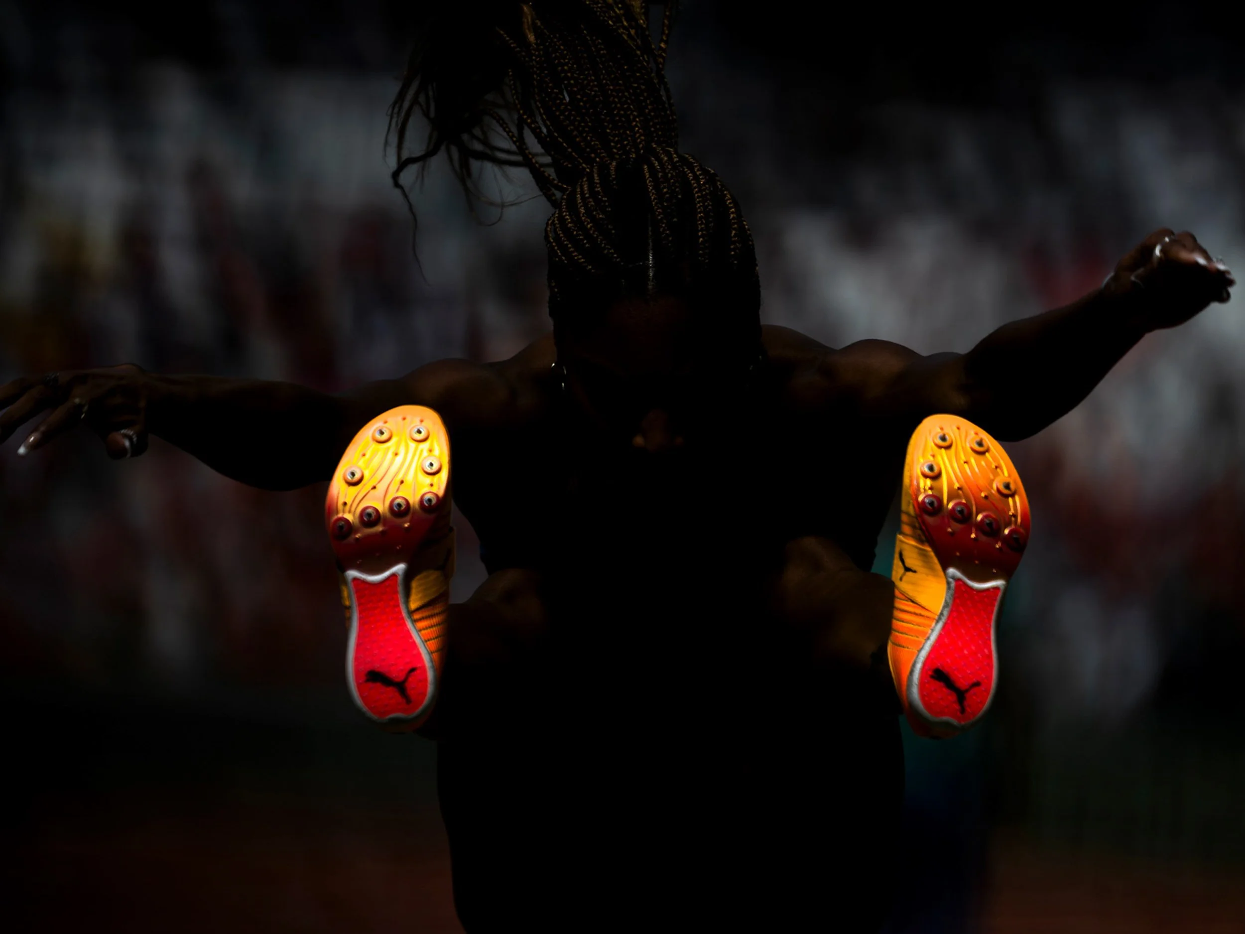 Athlete with braided hair stretching arms while wearing bright orange Puma athletic shoes