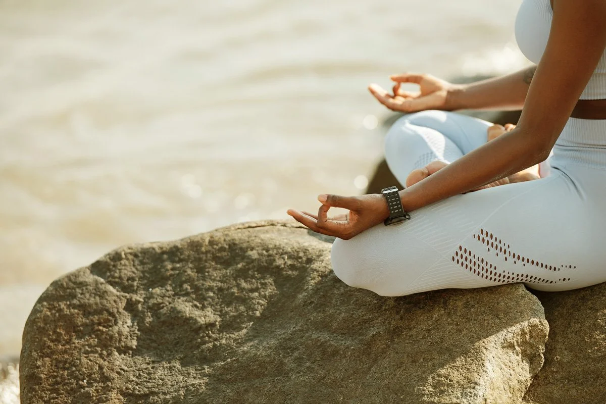 woman sitting on a rock next to water meditating