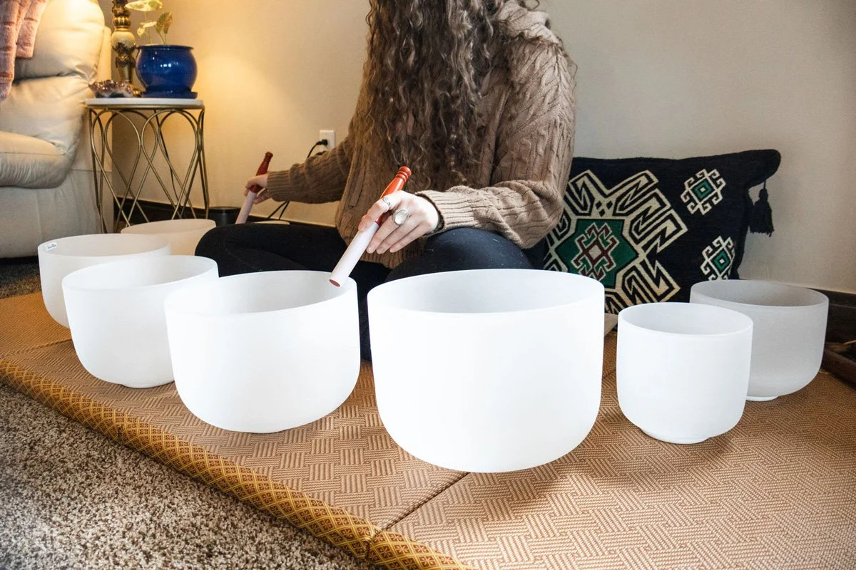Andiya playing crystal singing bowls on a mat indoors.