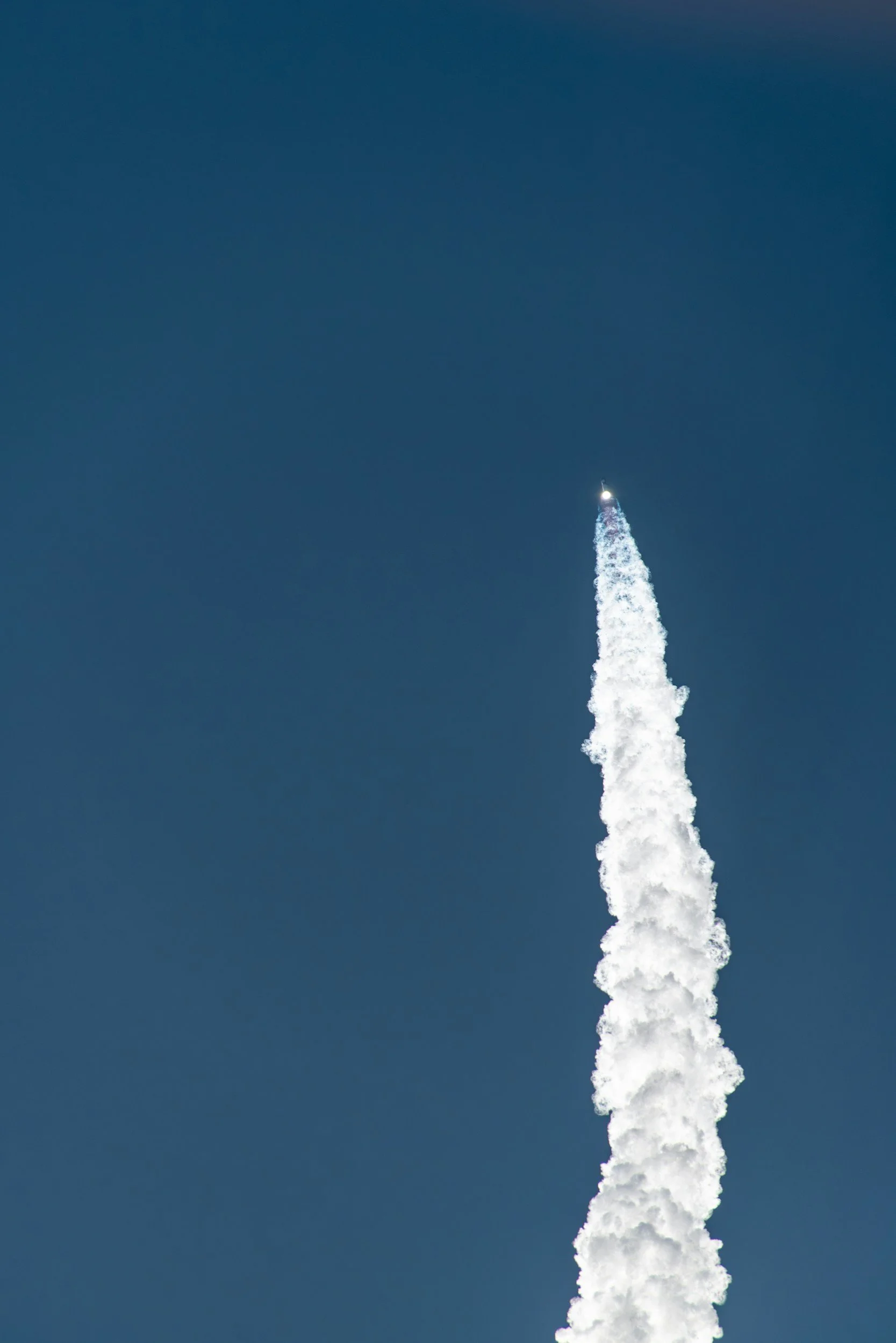 A rocket launching into the sky, leaving a trail of white smoke against a clear blue background.