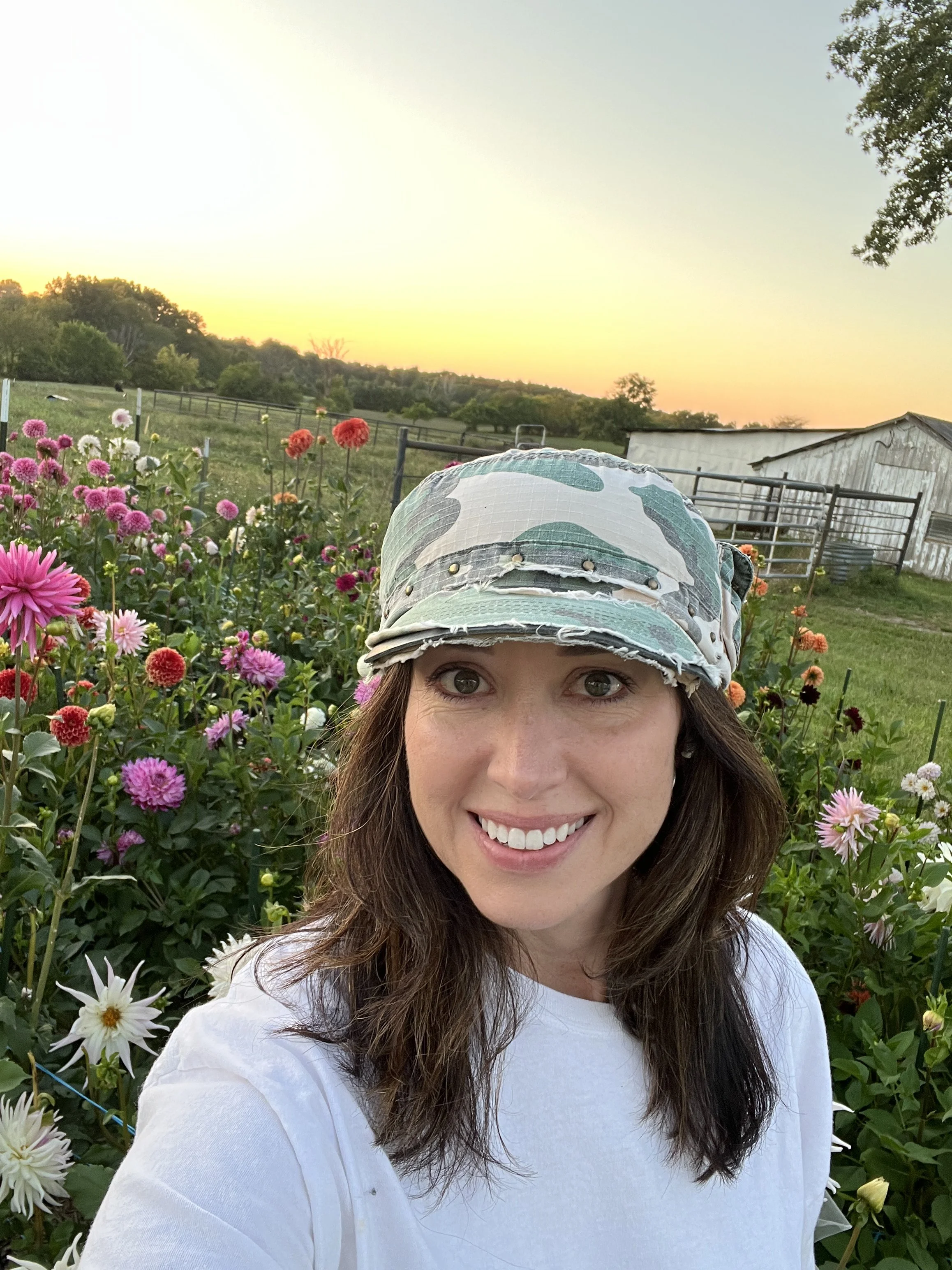 Farmer Amy Ferguson, AIFD standing in front of a field of brightly colored dahlia blooms at sunset.