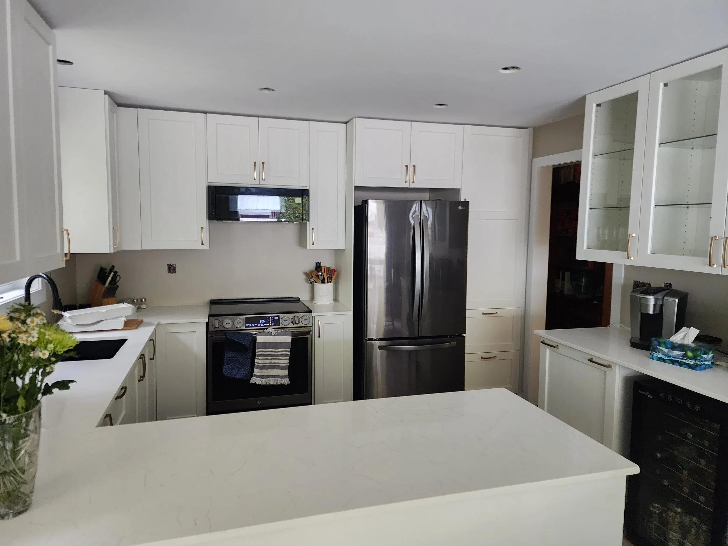 Modern kitchen with white cabinets, stainless steel refrigerator, stove, microwave, and a kitchen island with a white countertop.