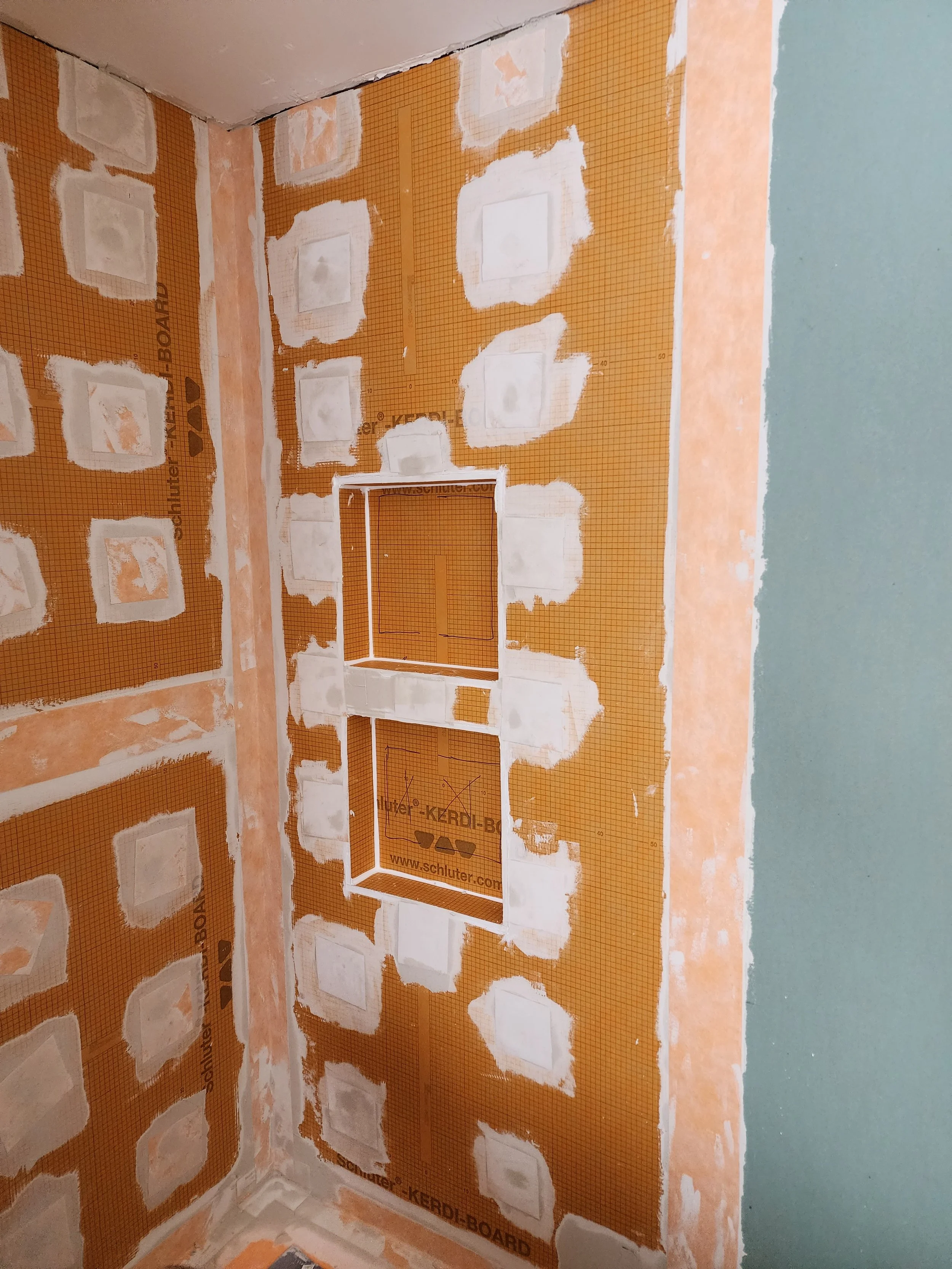 Bathroom wall with orange KERDI-BOARD and white drywall patches around an electrical outlet box opening.