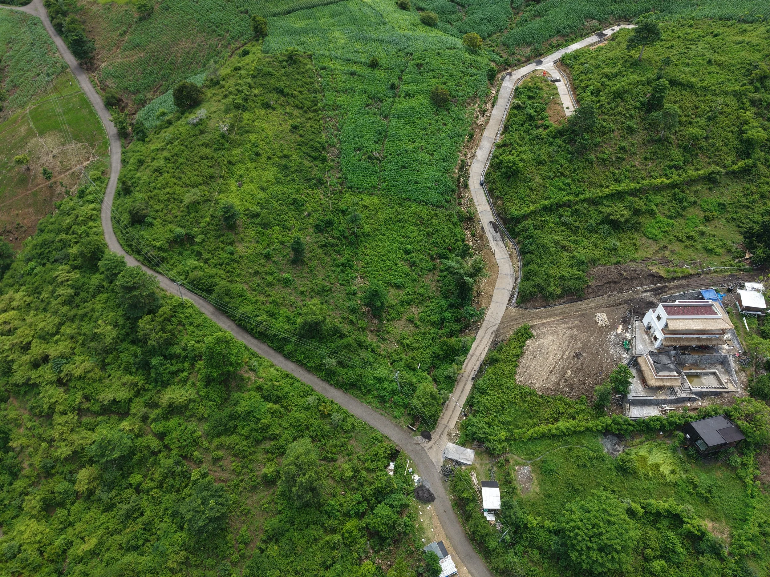 A winding concrete road through a lush green hilly landscape with scattered houses and farmland.