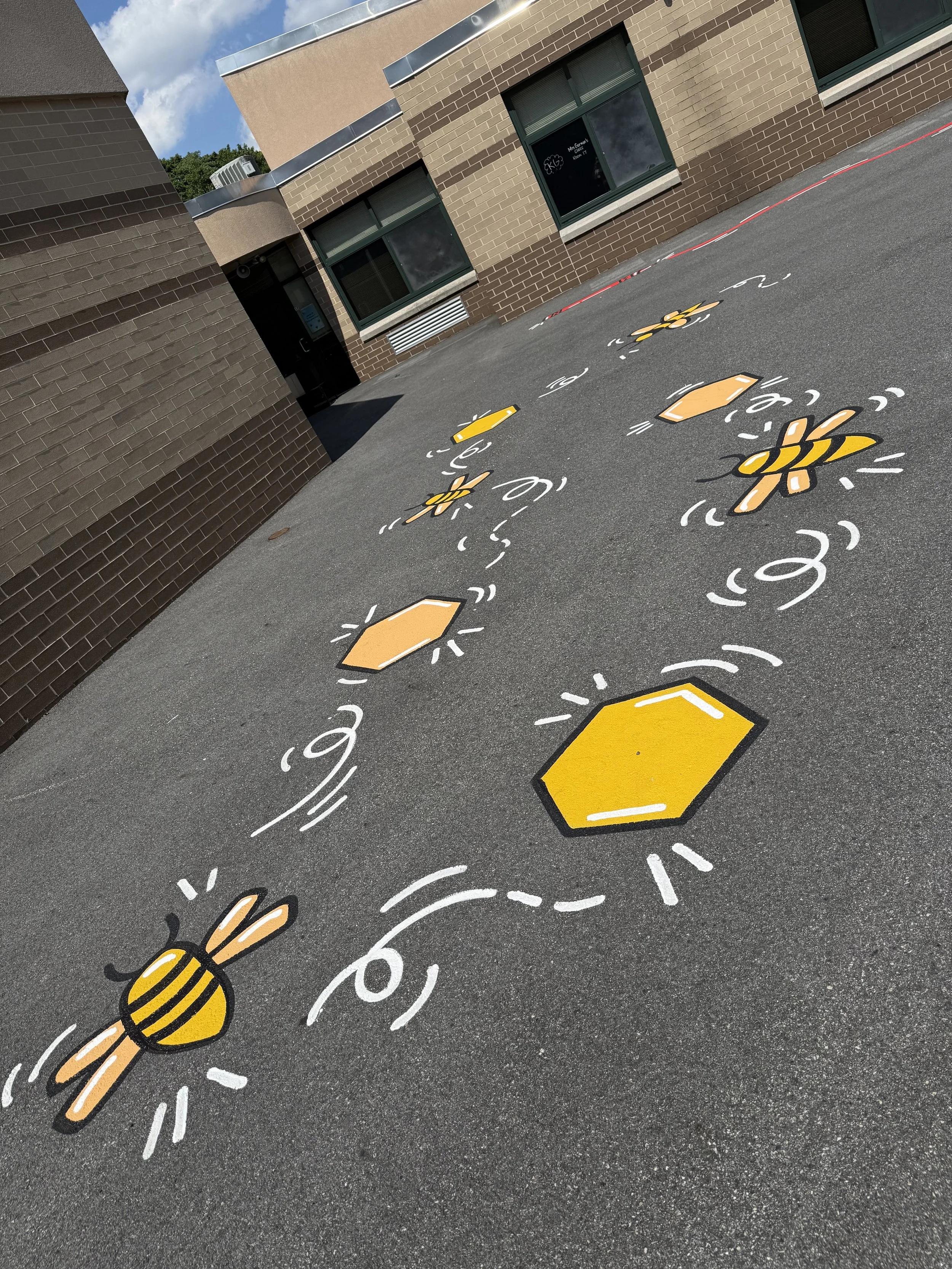 Outdoor school pavement mural featuring painted bees, honeycombs, and playful dotted pathways.