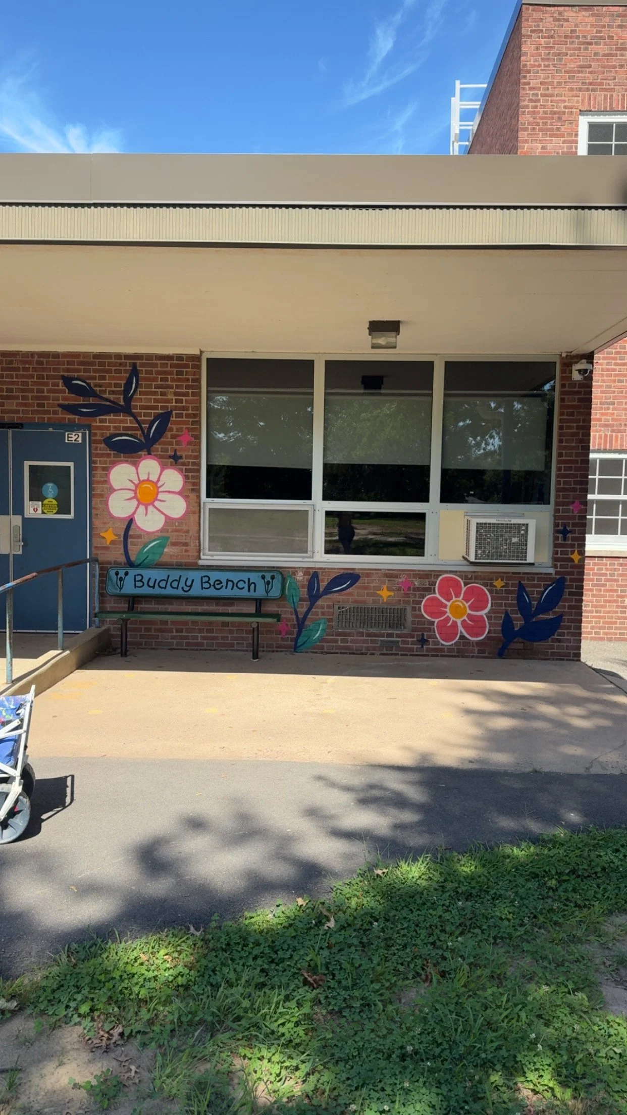 The exterior of a building with a mural of colorful flowers and the words "Buddy Bench."