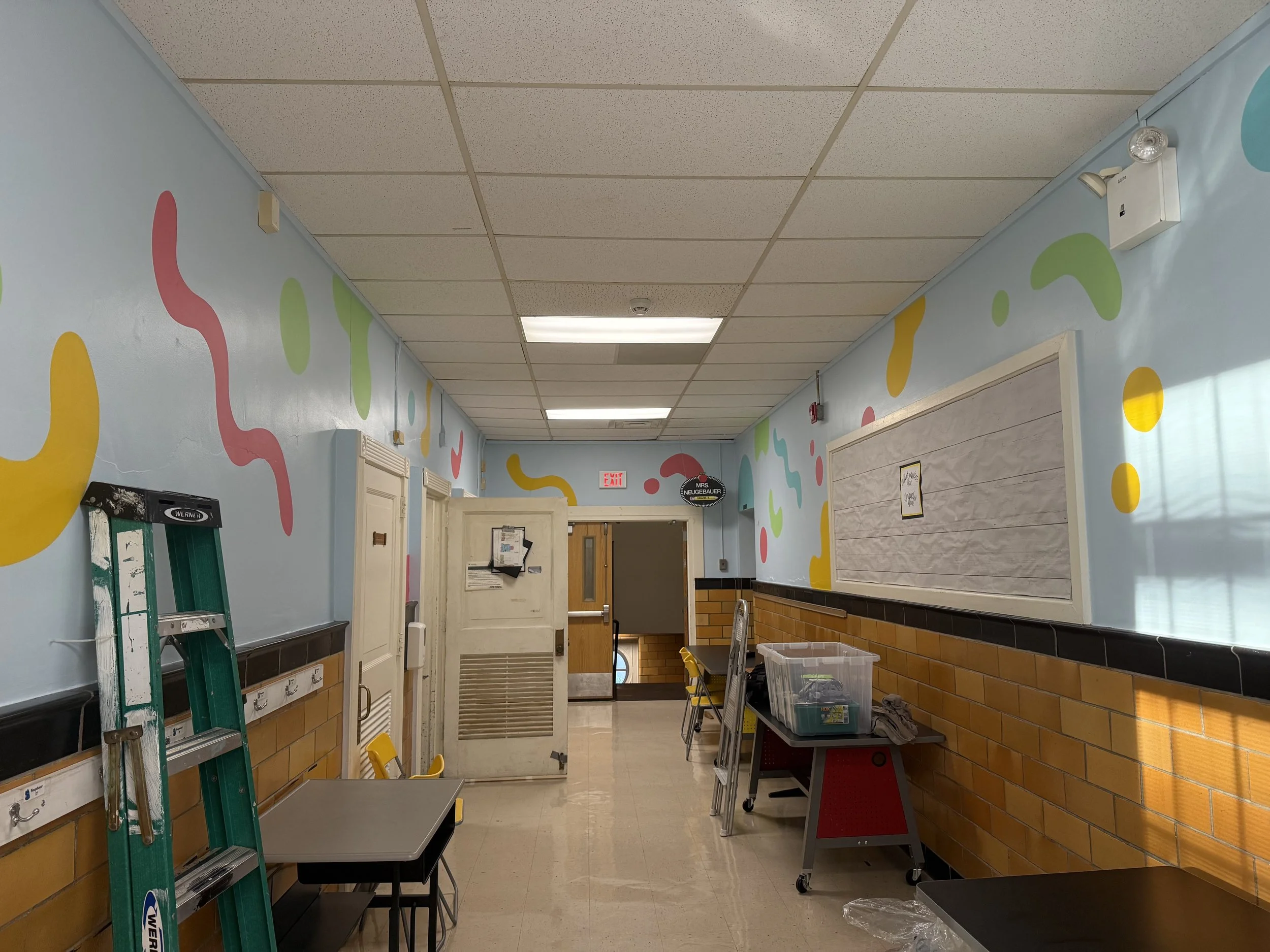 Interior school mural featuring colorful abstract shapes painted throughout a bright hallway.