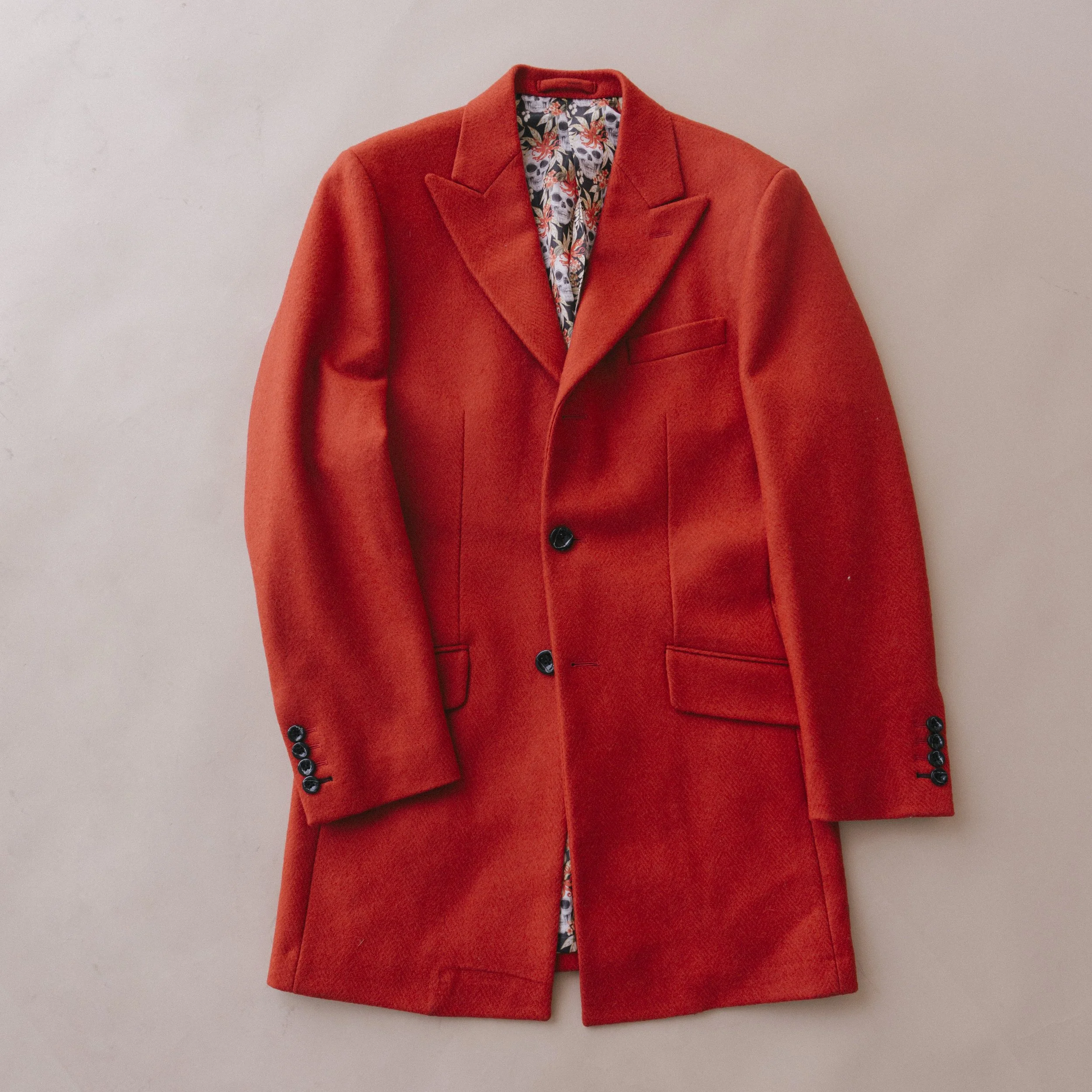 A red overcoat with a floral patterned lining, hanging against a plain background.