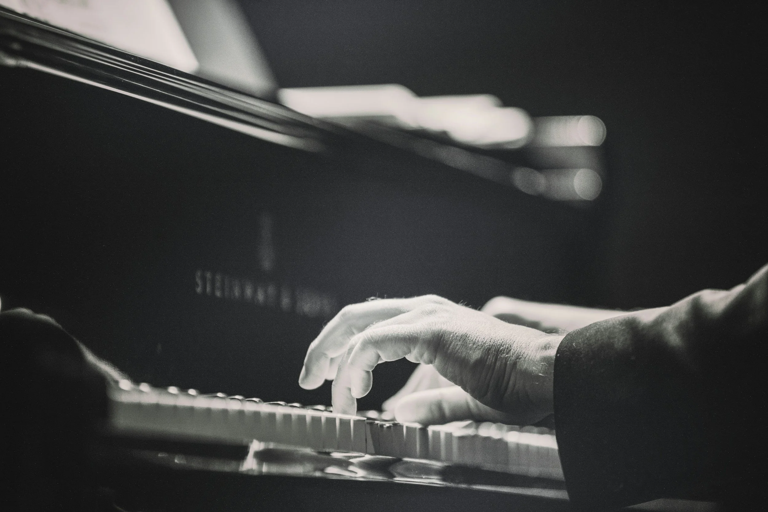 Close-up of hands playing a grand piano keyboard in low light