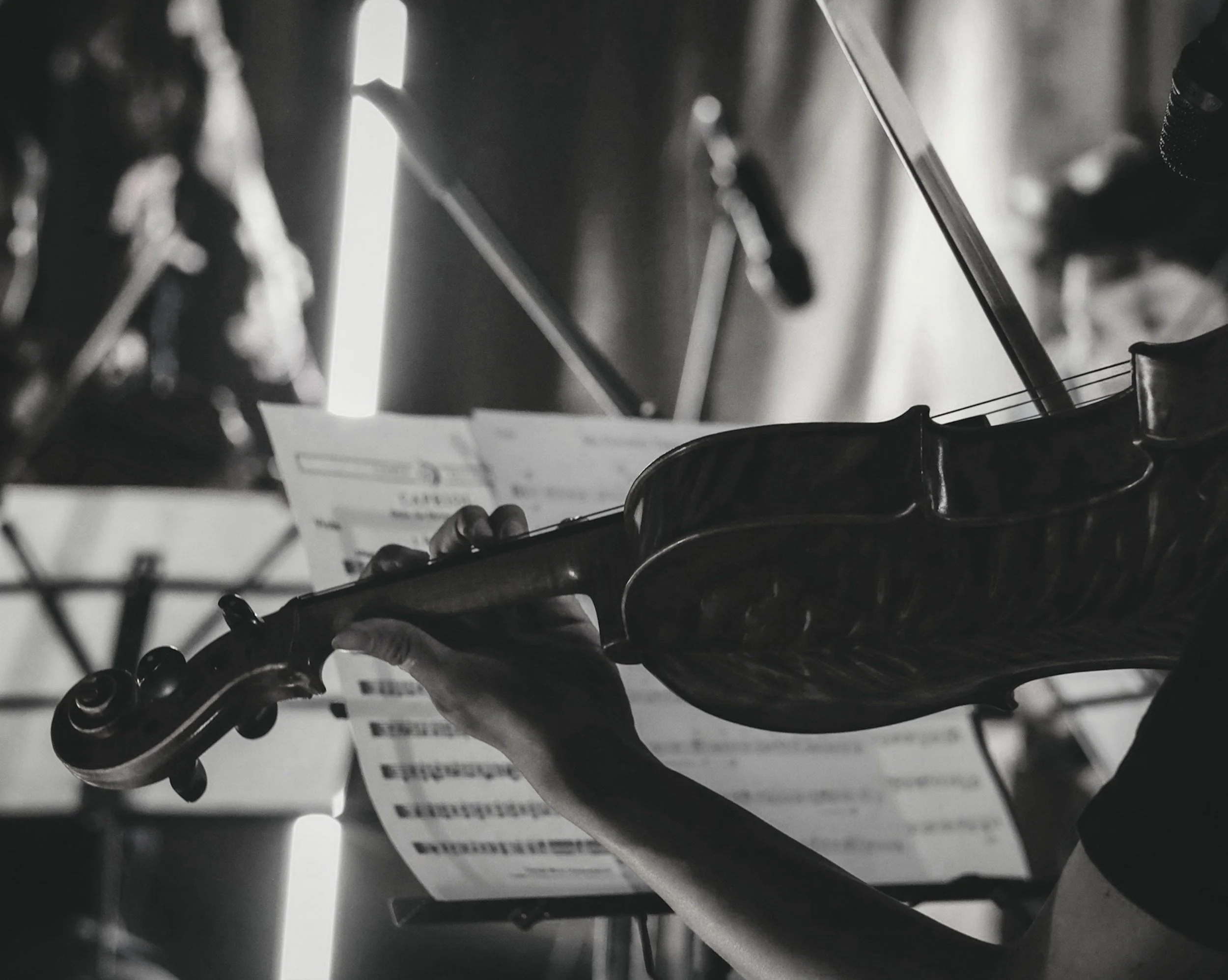 Close-up of violinist's hand playing a violin with sheet music in background, monochrome.