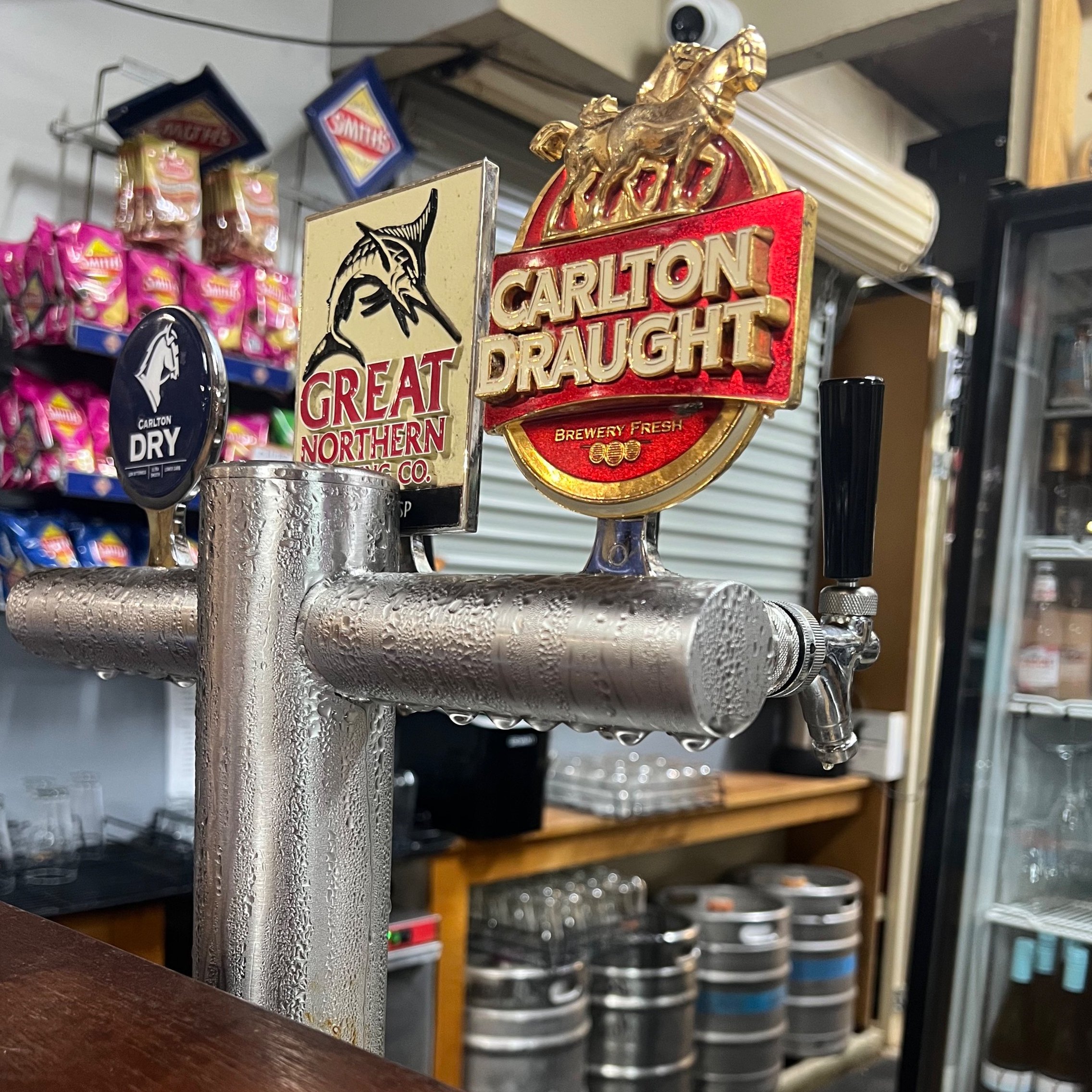 Cold beer tap with signs for Carlton Draught and Great Northern Brewing Co in a bar or setting.