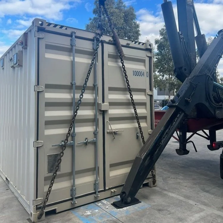 Gray shipping container secured with chains and machinery in an outdoor industrial area.