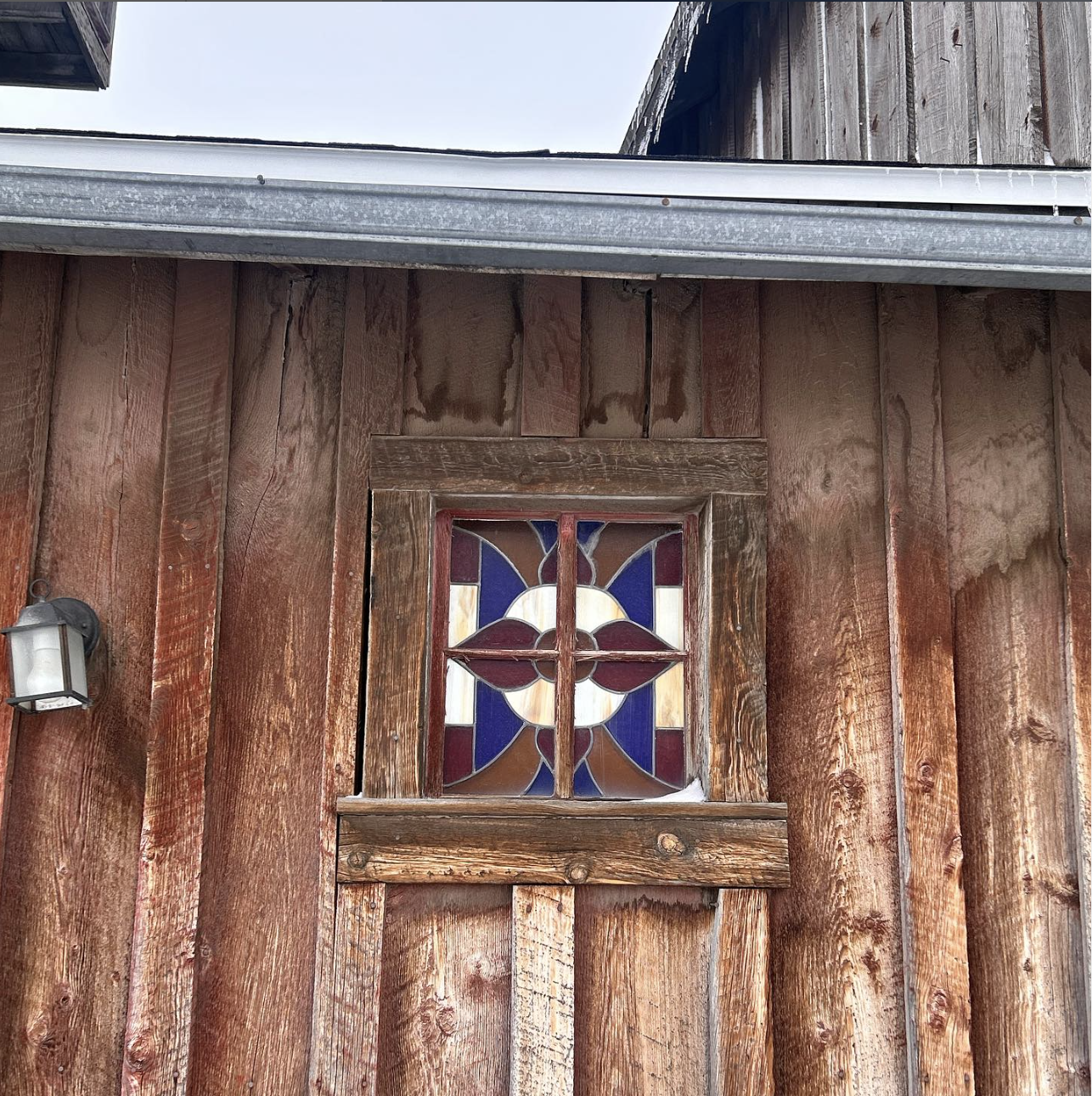 Exterior of a wooden building with decorative stained glass window and metal lamp