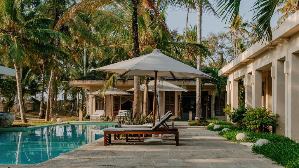 Poolside scene with lounge chairs and umbrellas, surrounded by palm trees and lush greenery.